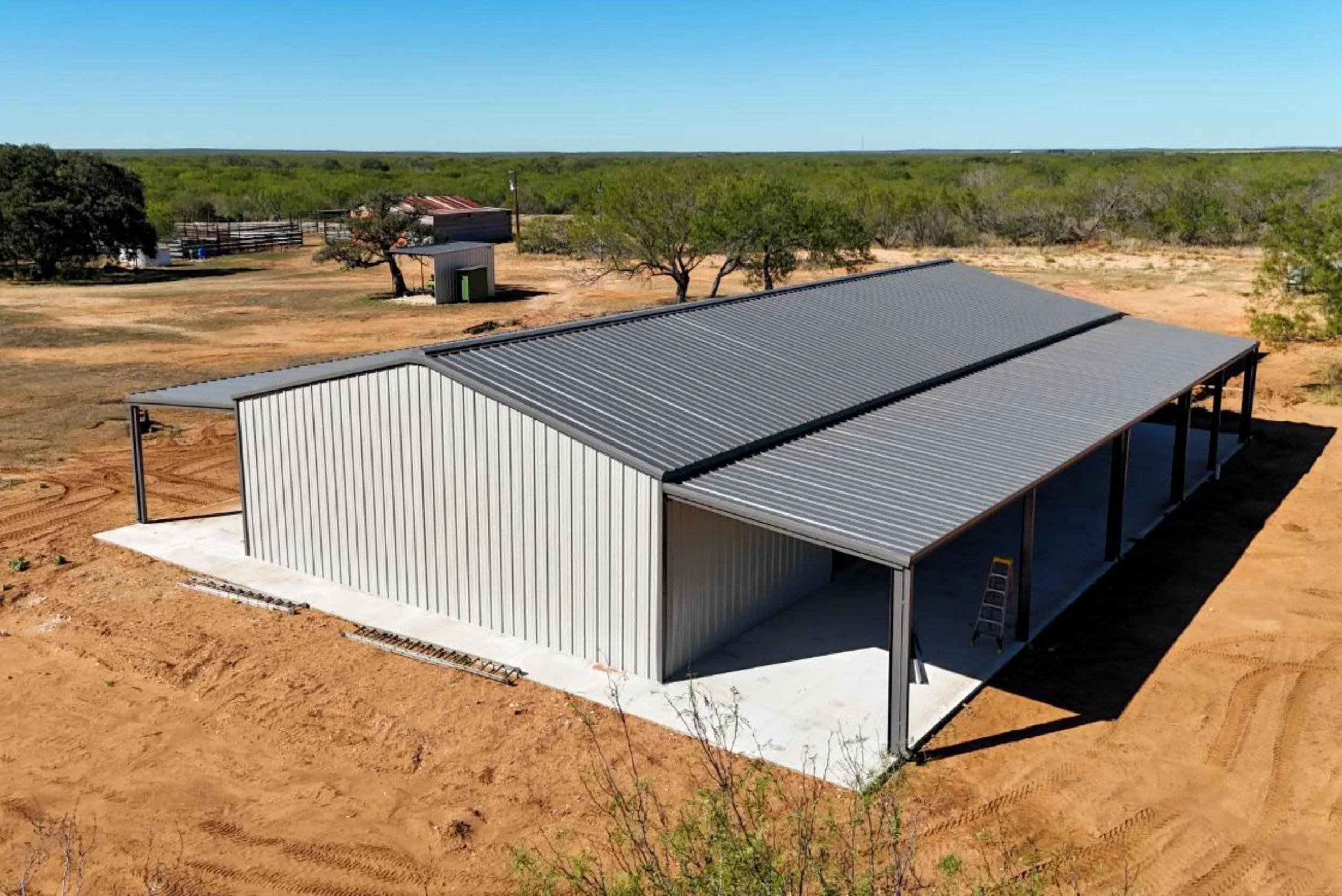 Backside view of insulated Mueller metal building barndominium in Bigfoot Texas with dark charcoal roof and lean-to overhang.