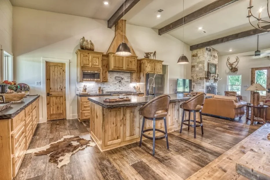 Custom barndominium kitchen featuring natural wood cabinetry, a large center island, stone countertops, pendant lighting, and exposed ceiling beams.