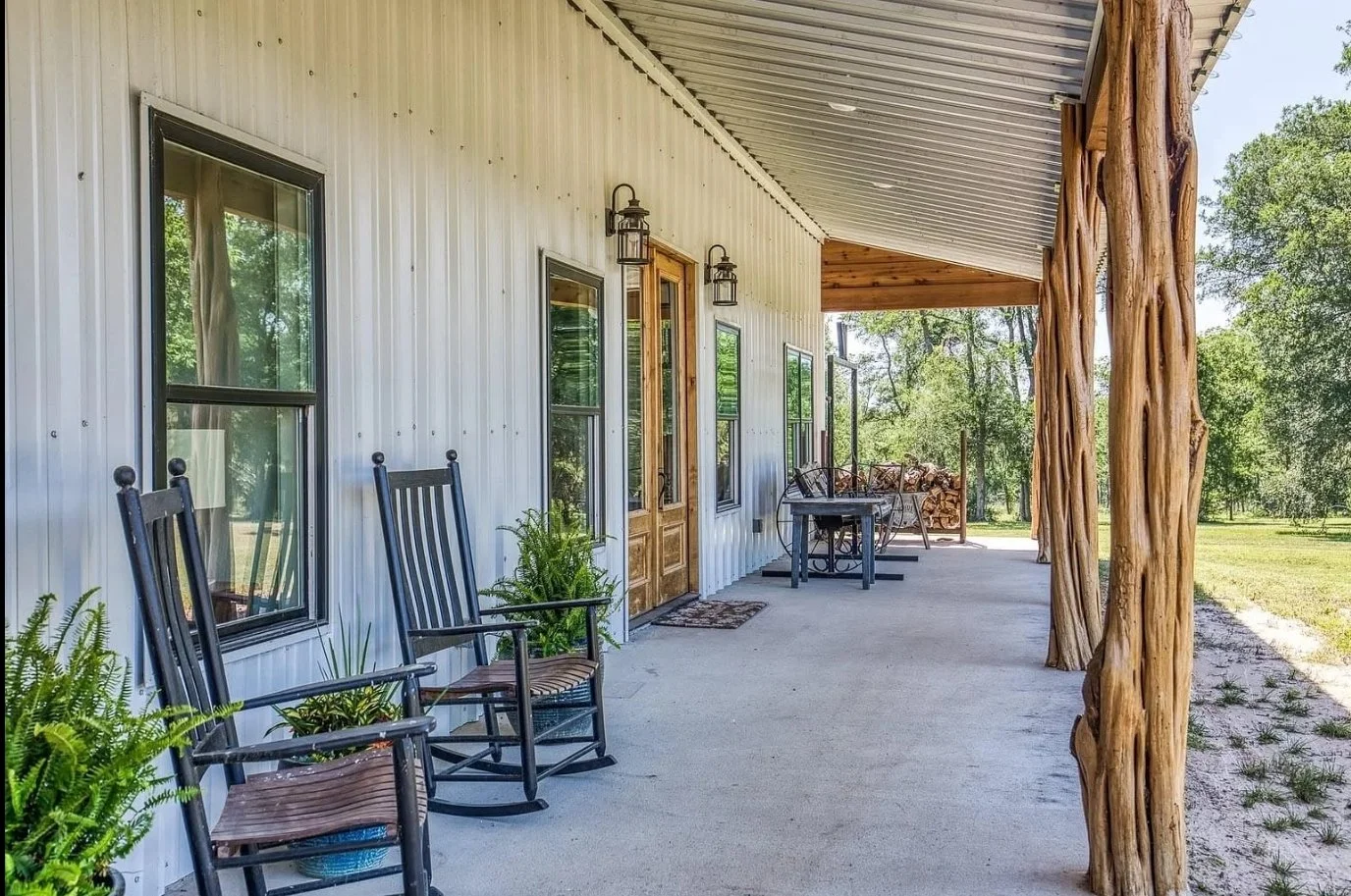 Spacious covered porch featuring natural cedar posts, metal siding, wood entry doors, and plenty of room for outdoor seating.