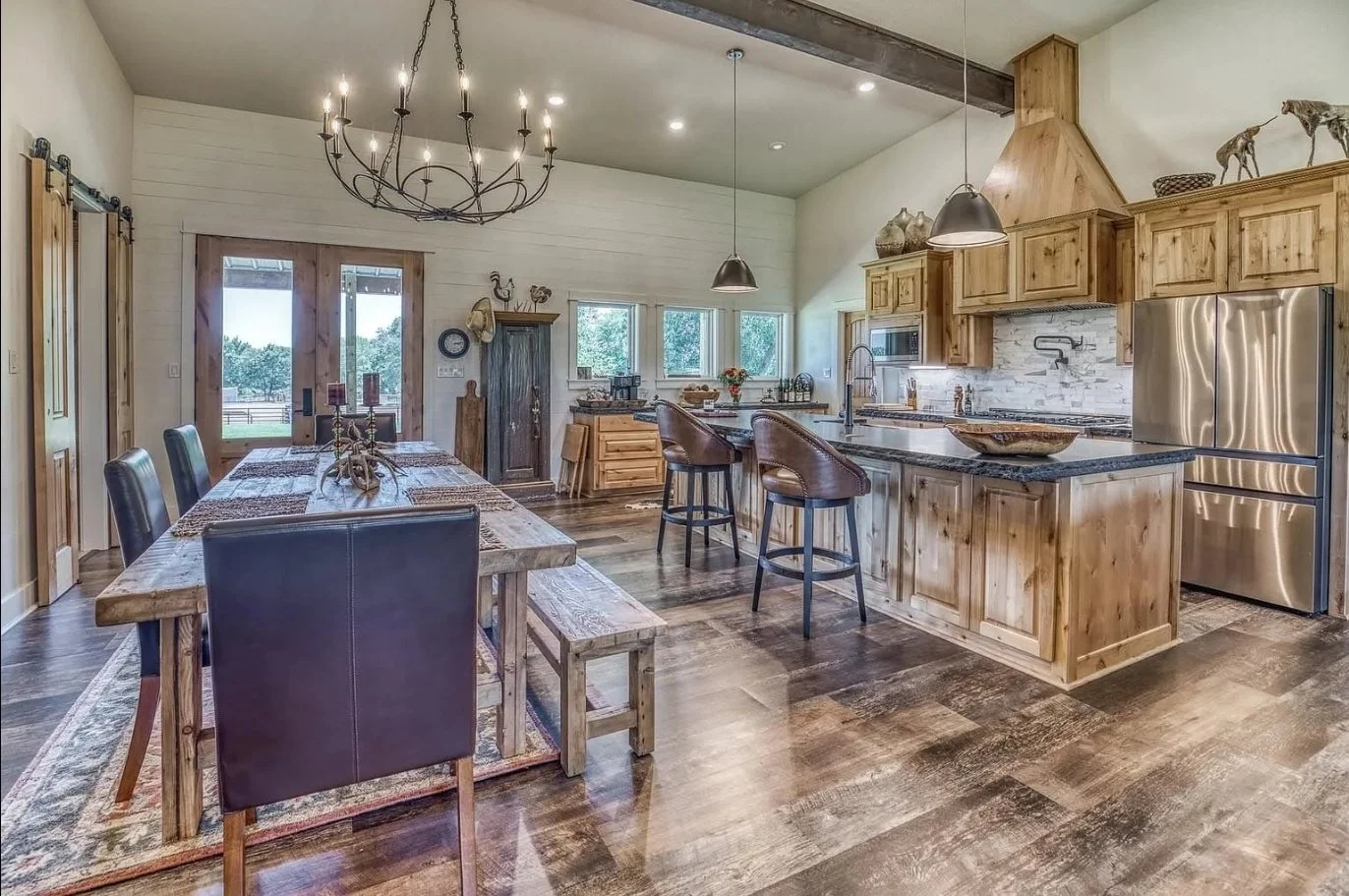 Open-concept kitchen and dining area with custom wood cabinetry, an oversized island with bar seating, rustic lighting, and wood-look flooring.