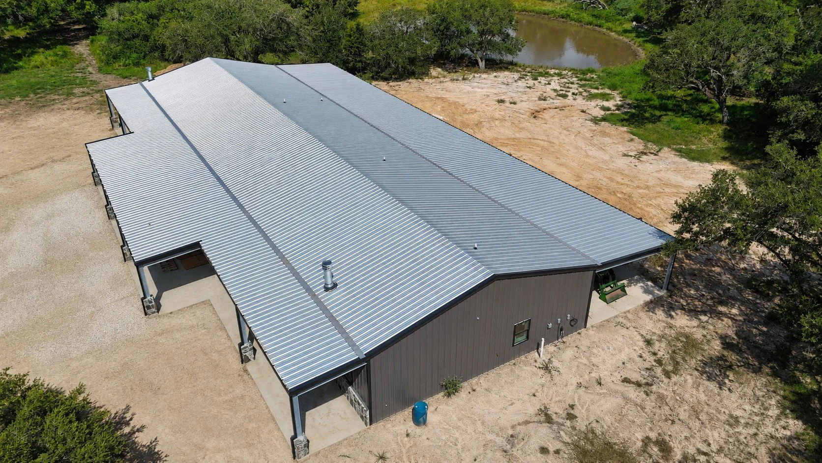 Overhead drone view showing the expansive Galvalume metal roof and the layout of the two residences connected by a shared shop and garage.