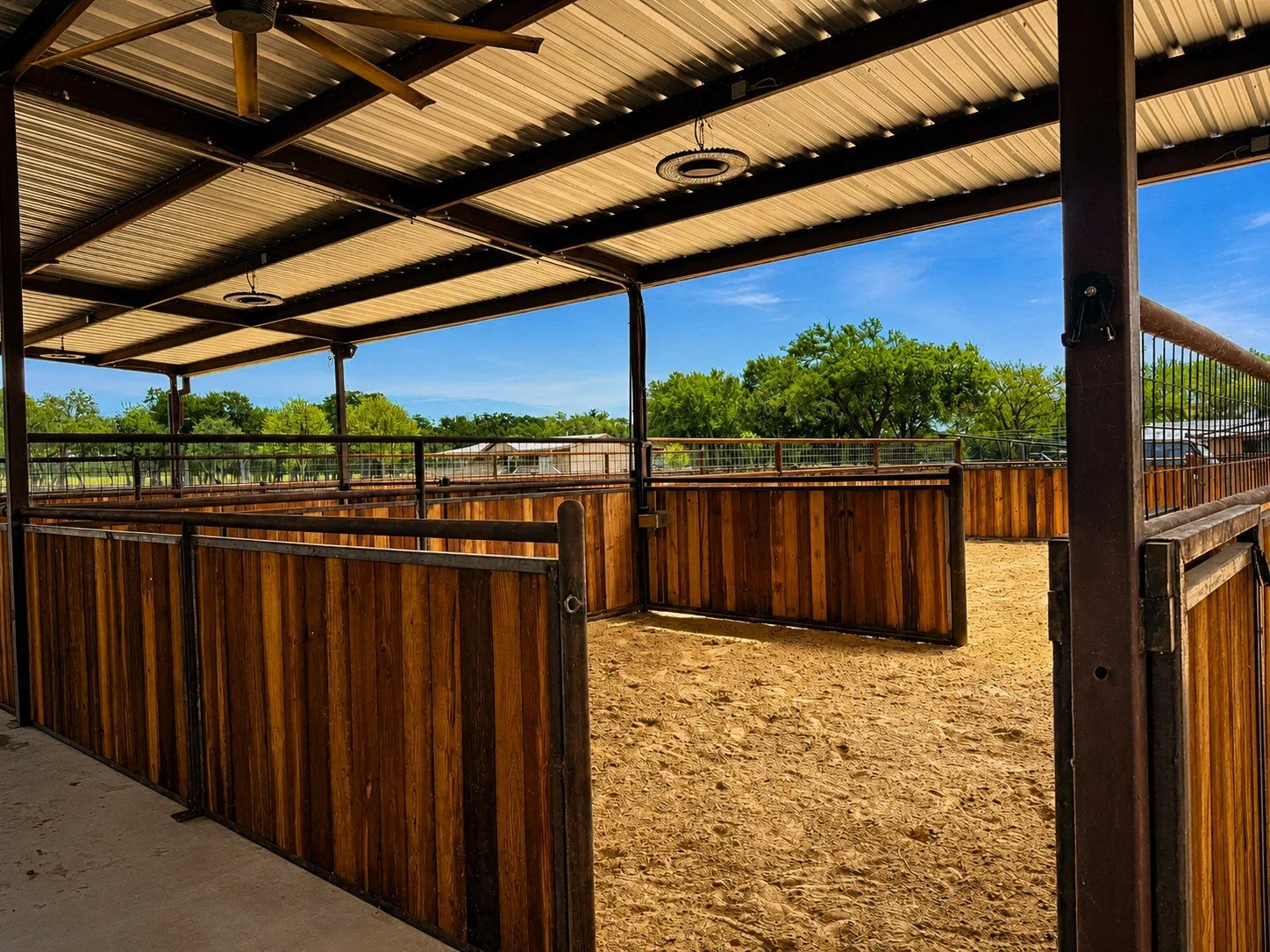Spacious custom horse stall with welded steel construction and creosote wood panels beneath a covered barn in Caldwell, TX.