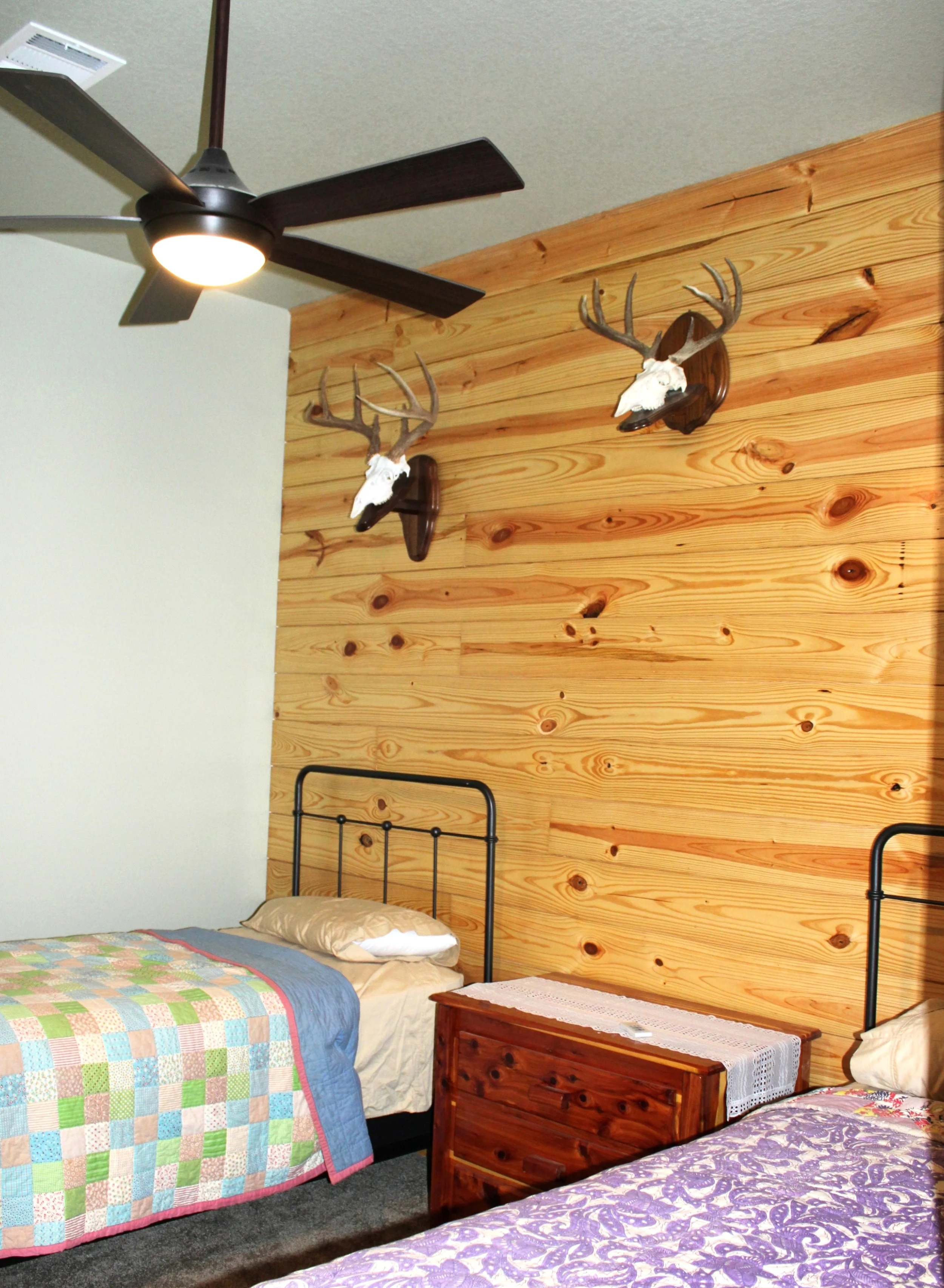 Guest bedroom inside South Texas hunting barndominium with twin beds and wood accent wall with mounted deer horns.