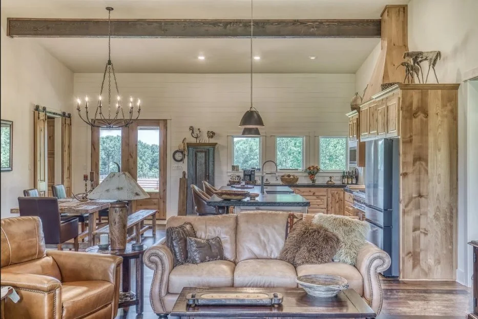 Open-concept living area overlooking the kitchen and dining space, with exposed beams, high ceilings, custom cabinetry, and abundant natural light.