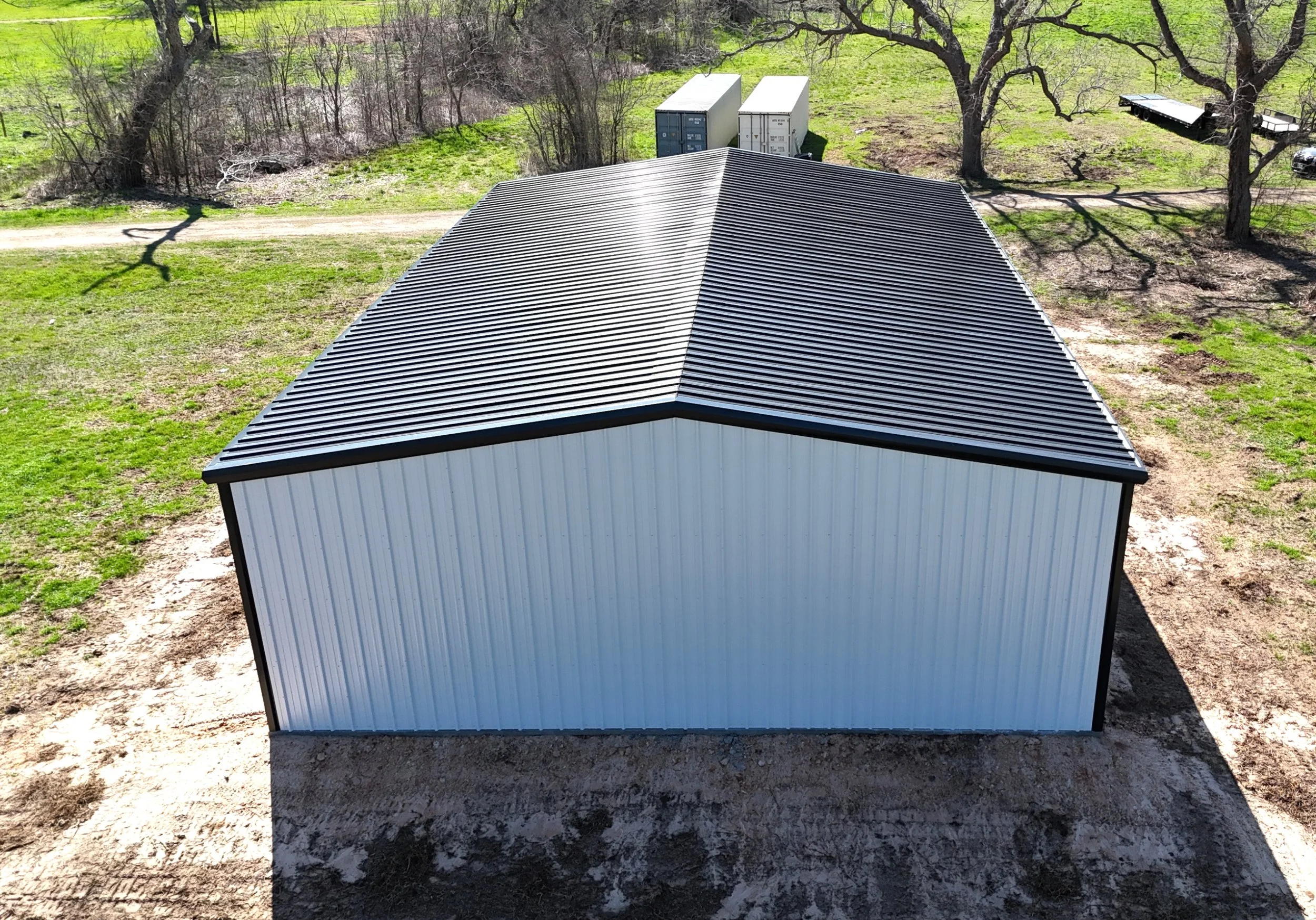 Rear view of custom white metal shop with black roof in Fulshear, Texas showing clean panel installation and gutter system for water runoff management.