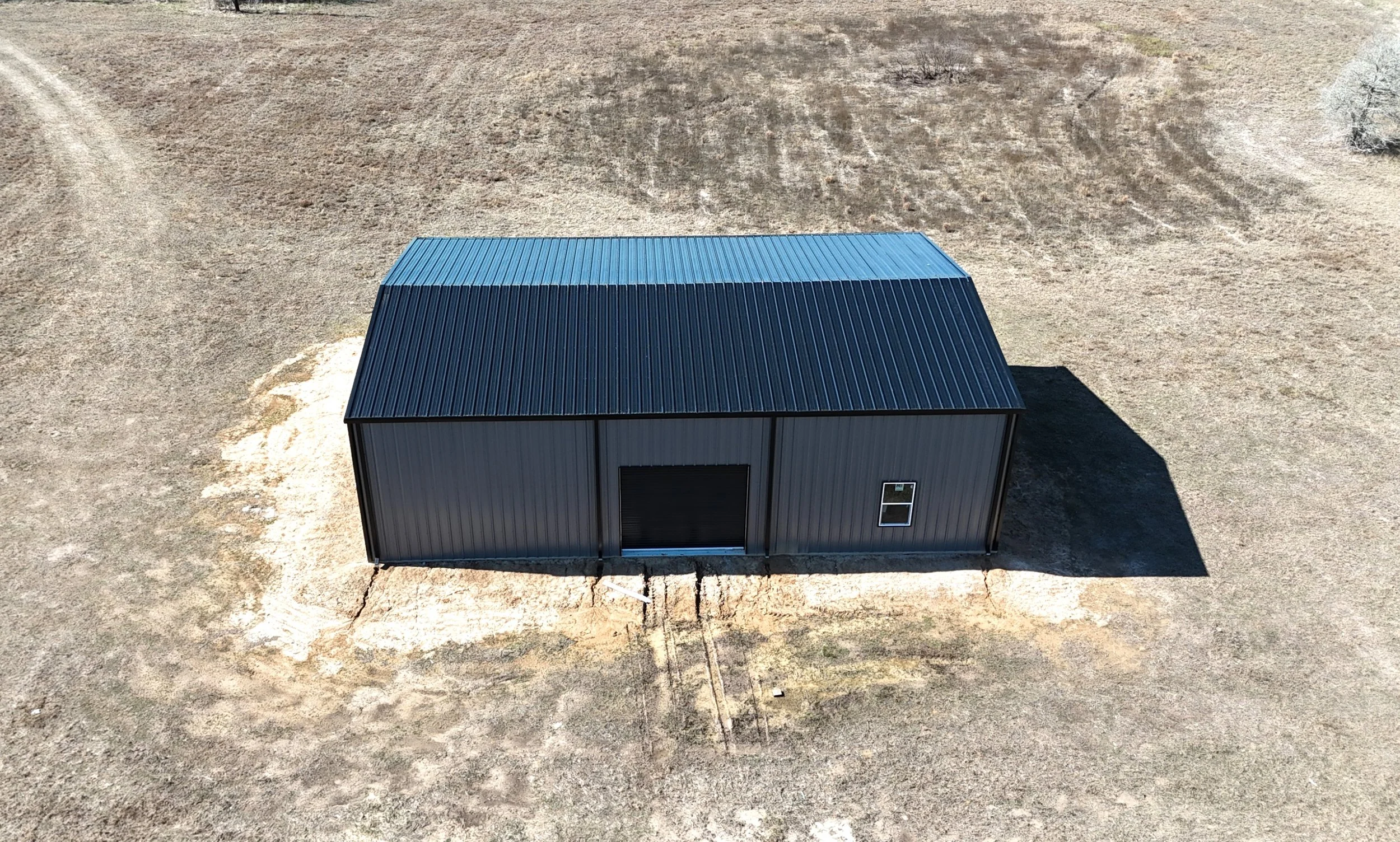 Exterior angle of a custom insulated metal shop in Wallis, TX highlighting black roof, gutters, and durable construction for long-term performance.