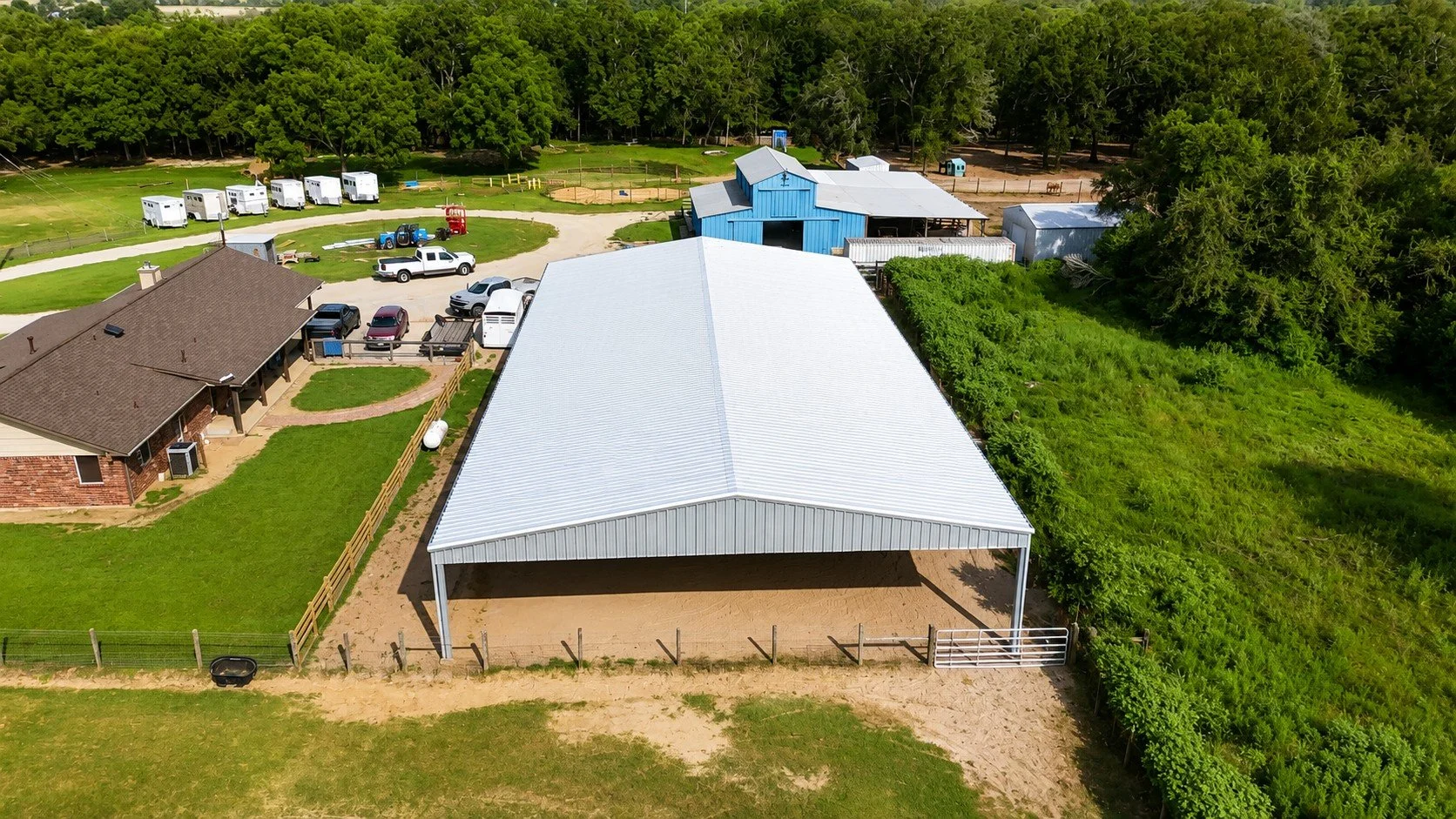 Aerial drone view showcasing the Galvalume roof and steel frame of a custom covered riding arena in Needville, Texas.