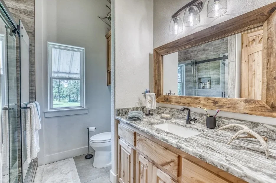 Secondary bathroom featuring a custom wood vanity, stone countertop, large framed mirror, and glass-enclosed walk-in shower.