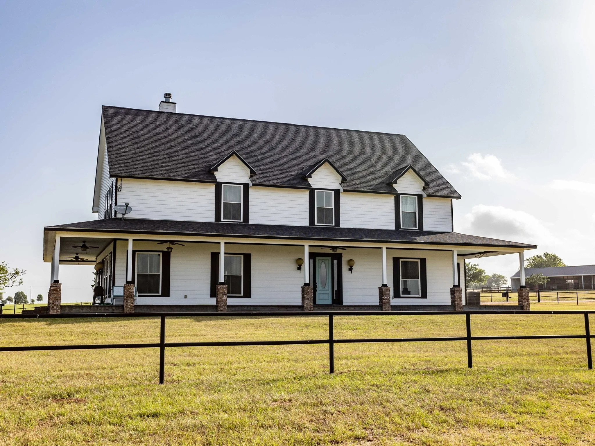 This custom-built home sits on a beautiful acreage in New Ulm, Texas, complete with a wrap-around porch, attached carport, pool, hot tub, and sweeping countryside views.