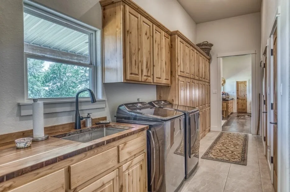 Spacious laundry room and mudroom featuring custom cabinetry, a utility sink, generous storage, and durable tile flooring.