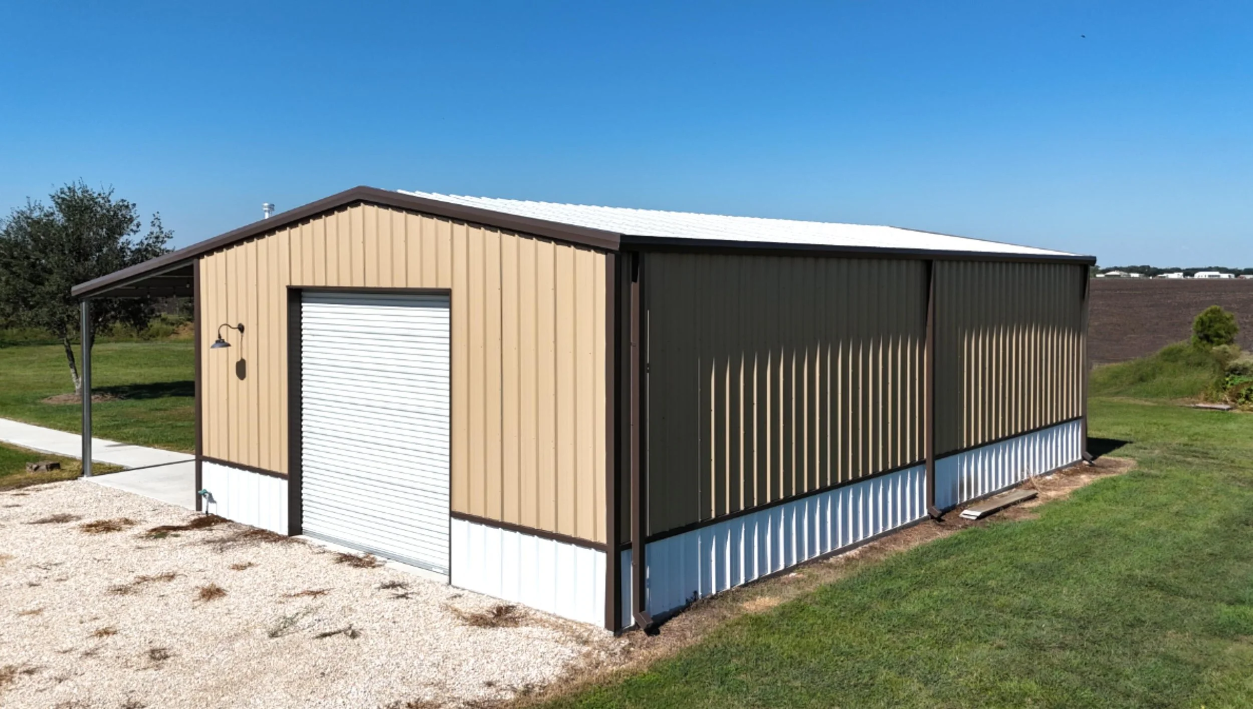 Custom 30x50 metal shop and garage with 15x50 covered porch, built in Fort Bend County, Texas, featuring multiple roll-up doors, white wainscot, matching metal well house, and concrete walkway connecting to the home.
