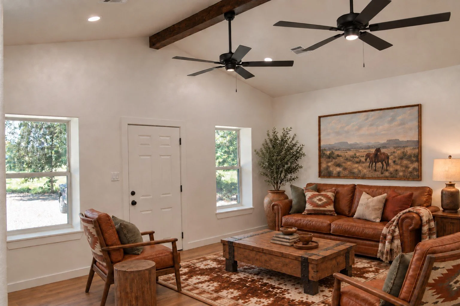 Vaulted barndominium living room featuring exposed wood beams, black ceiling fans, large windows, and warm rustic furnishings.