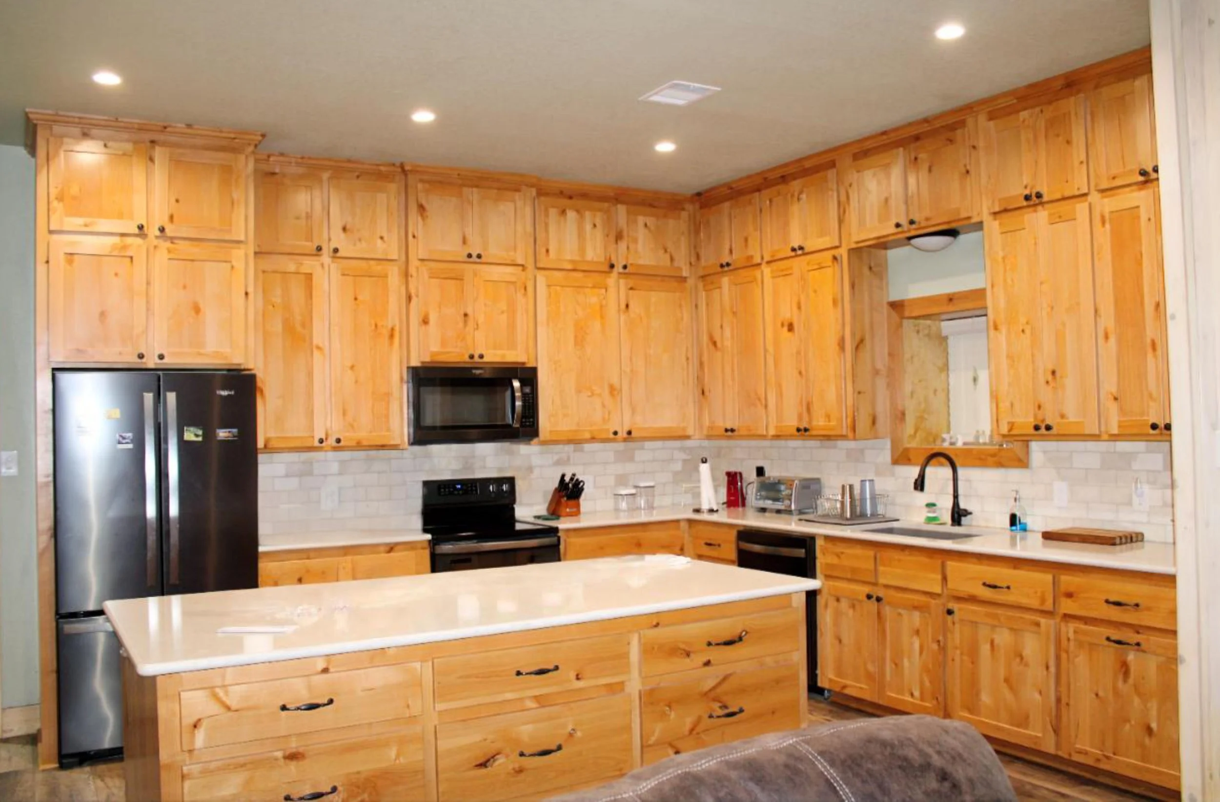 Custom rustic kitchen inside metal barndominium with knotty natural wood cabinets, stone backsplash, and appliances.