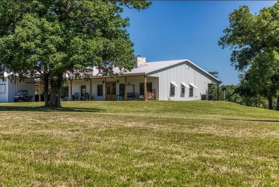 Exterior view of the custom metal barndominium and horse barn situated among mature trees in the Washington County countryside.