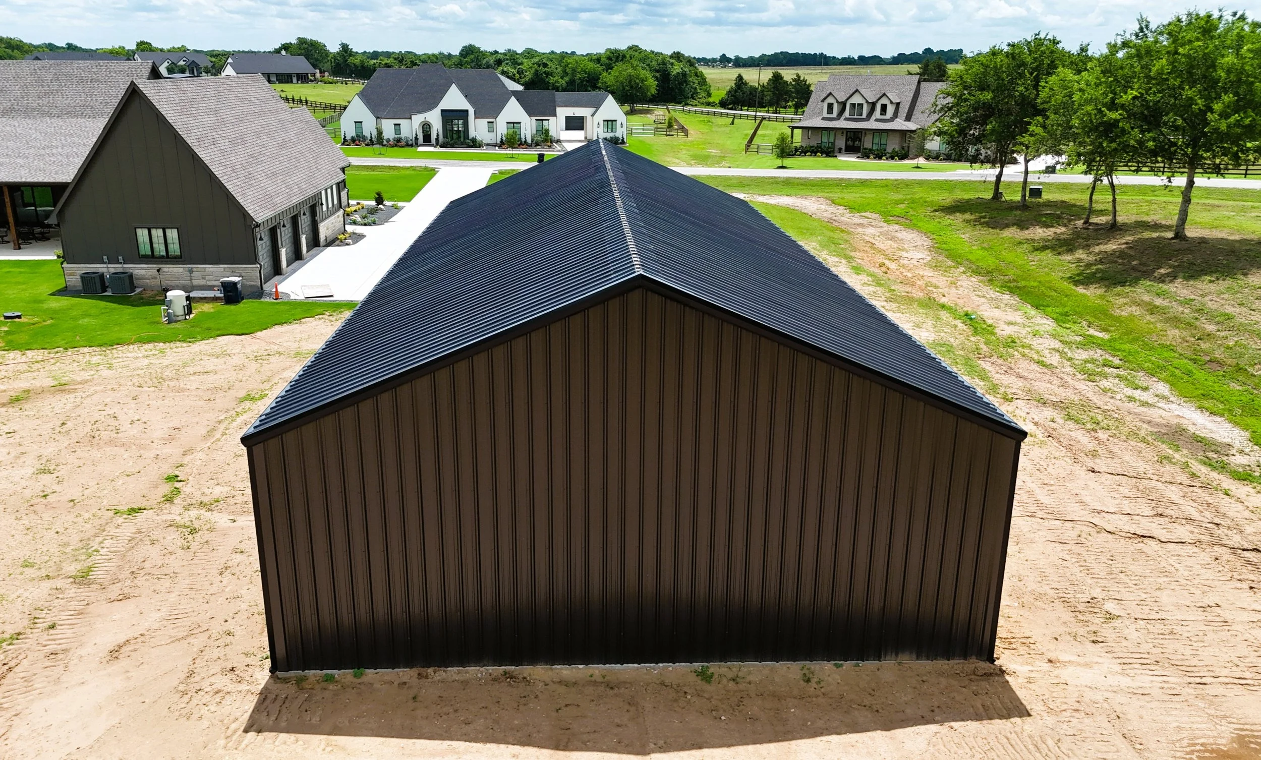 Rear aerial view of custom steel shop building in Chappell Hill, TX highlighting the symmetrical 5/12 roof pitch, black standing seam style roof appearance, and clean modern exterior finish.