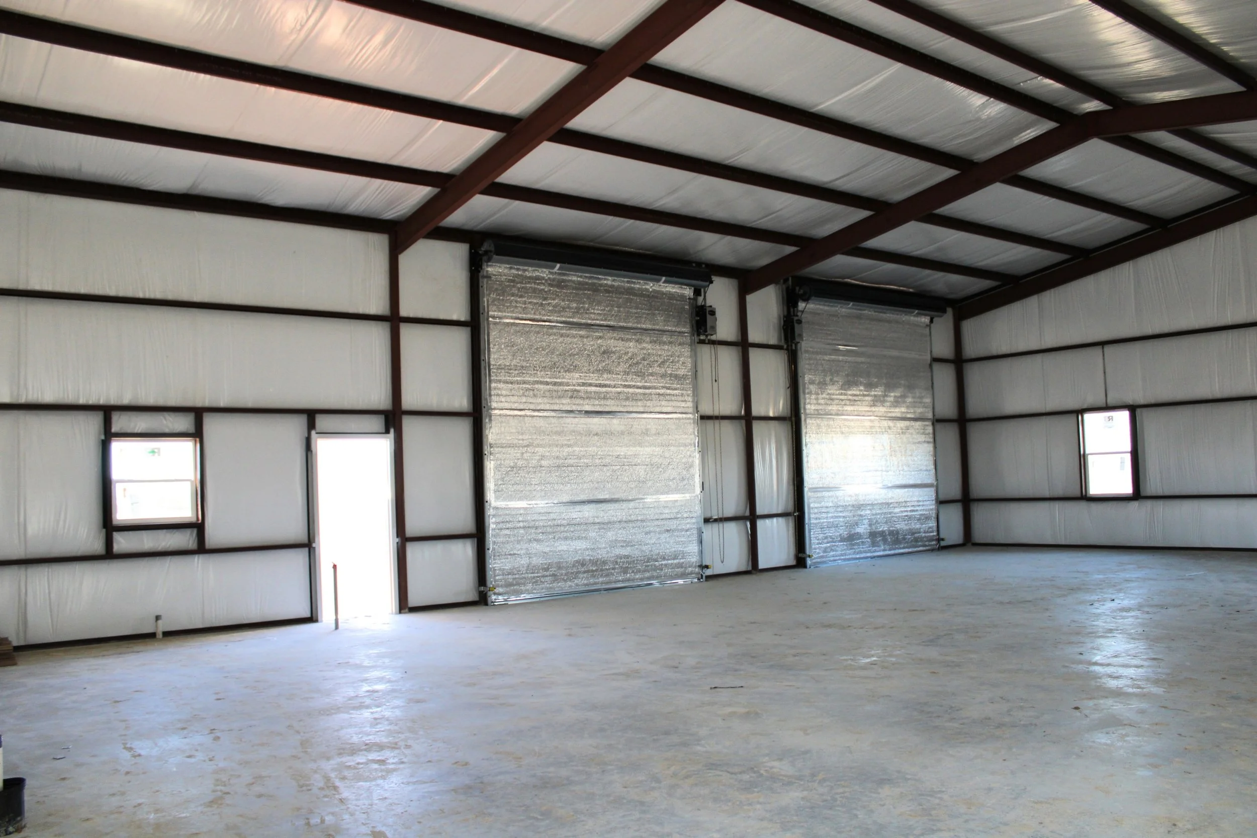 Interior of a fully insulated metal shop in Wallis, TX featuring open-span steel framing, high ceilings, and a spacious concrete floor for versatile shop use.