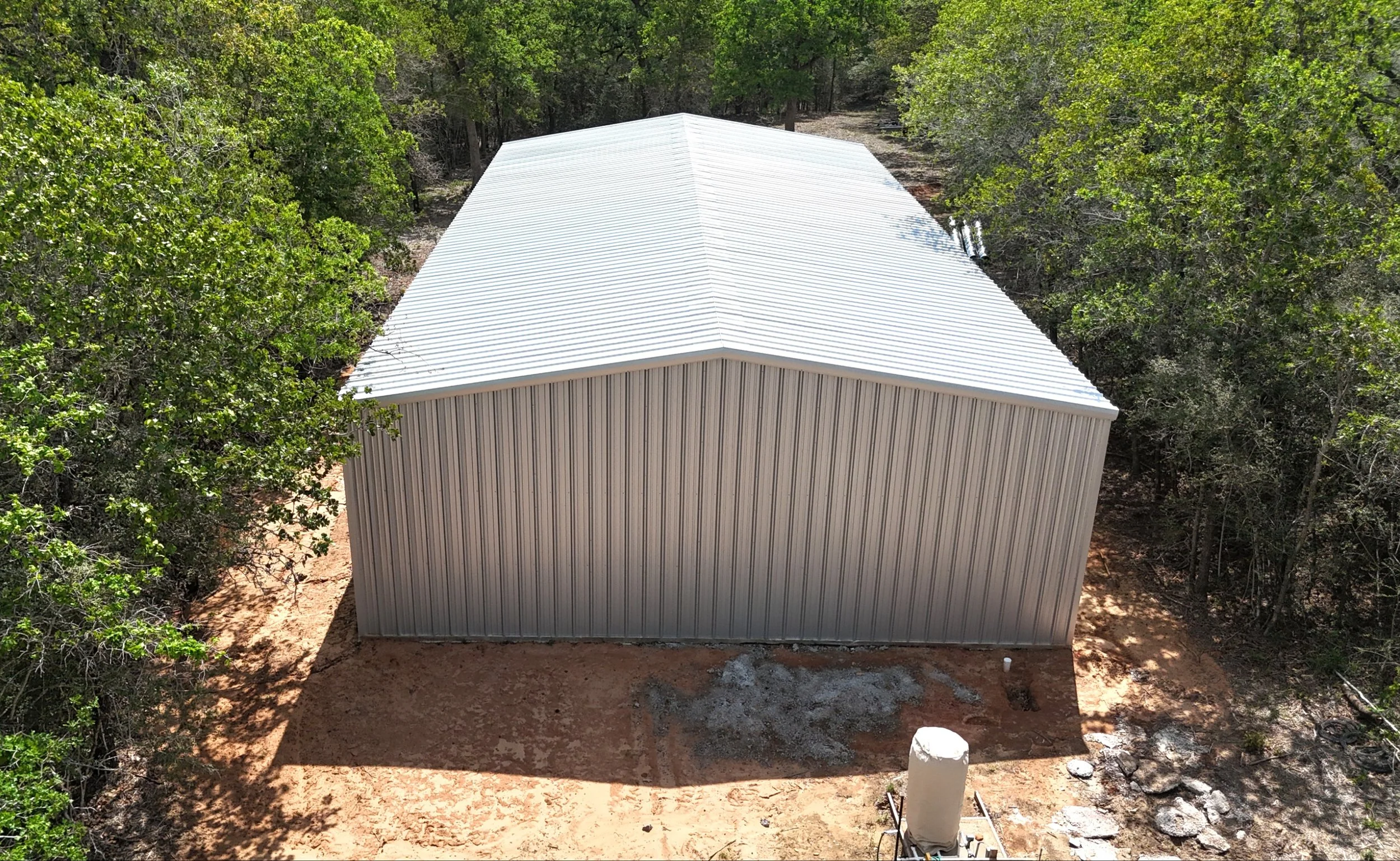 Rear aerial view of 40x60 custom metal shop with Galvalume siding and roof surrounded by wooded property in South Texas