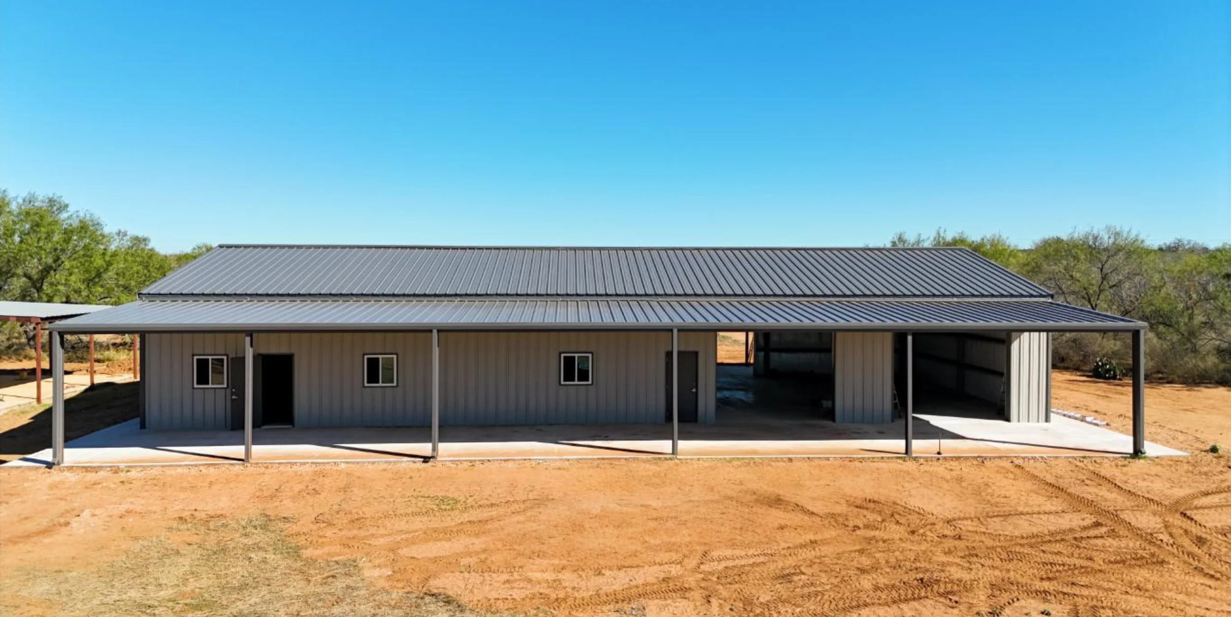 Covered lean-to porch space on metal barndominium with walk doors and windows, showing shade structure supported by steel posts.