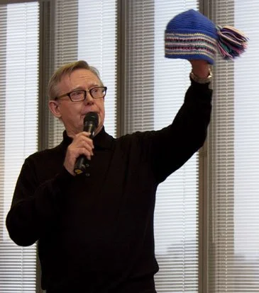 Photo of Bob speaking while holding up a hat