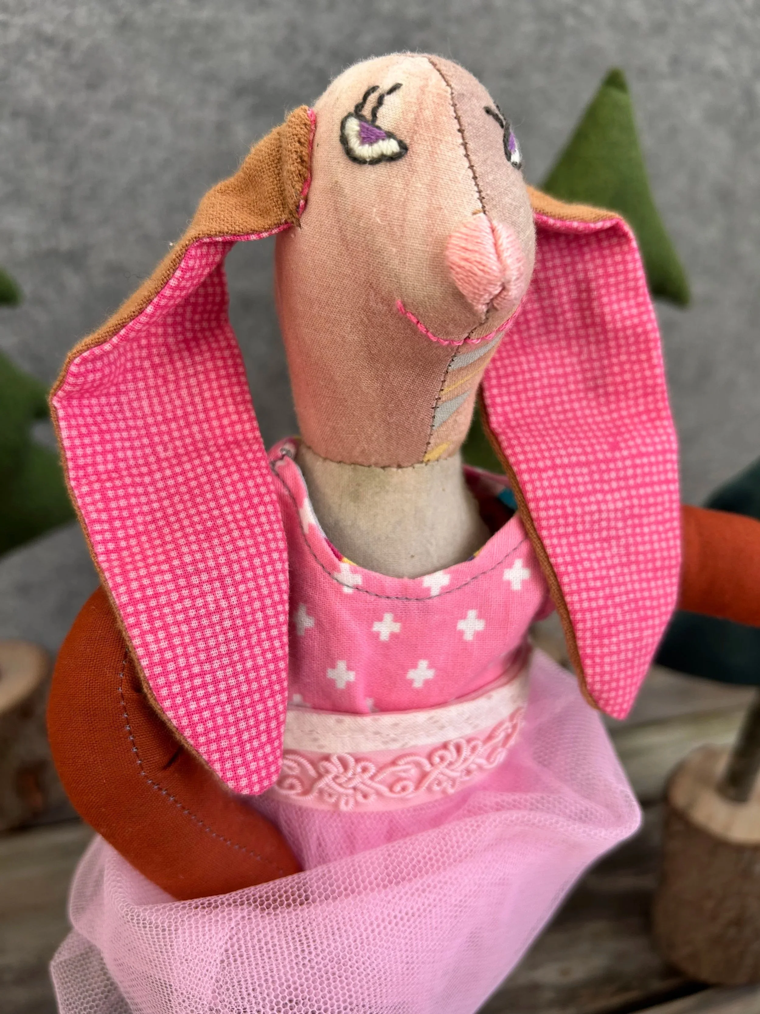 A handmade bunny with an embroidered face. It is wearing a pink leotard with white cross patterns and a pink tutu.