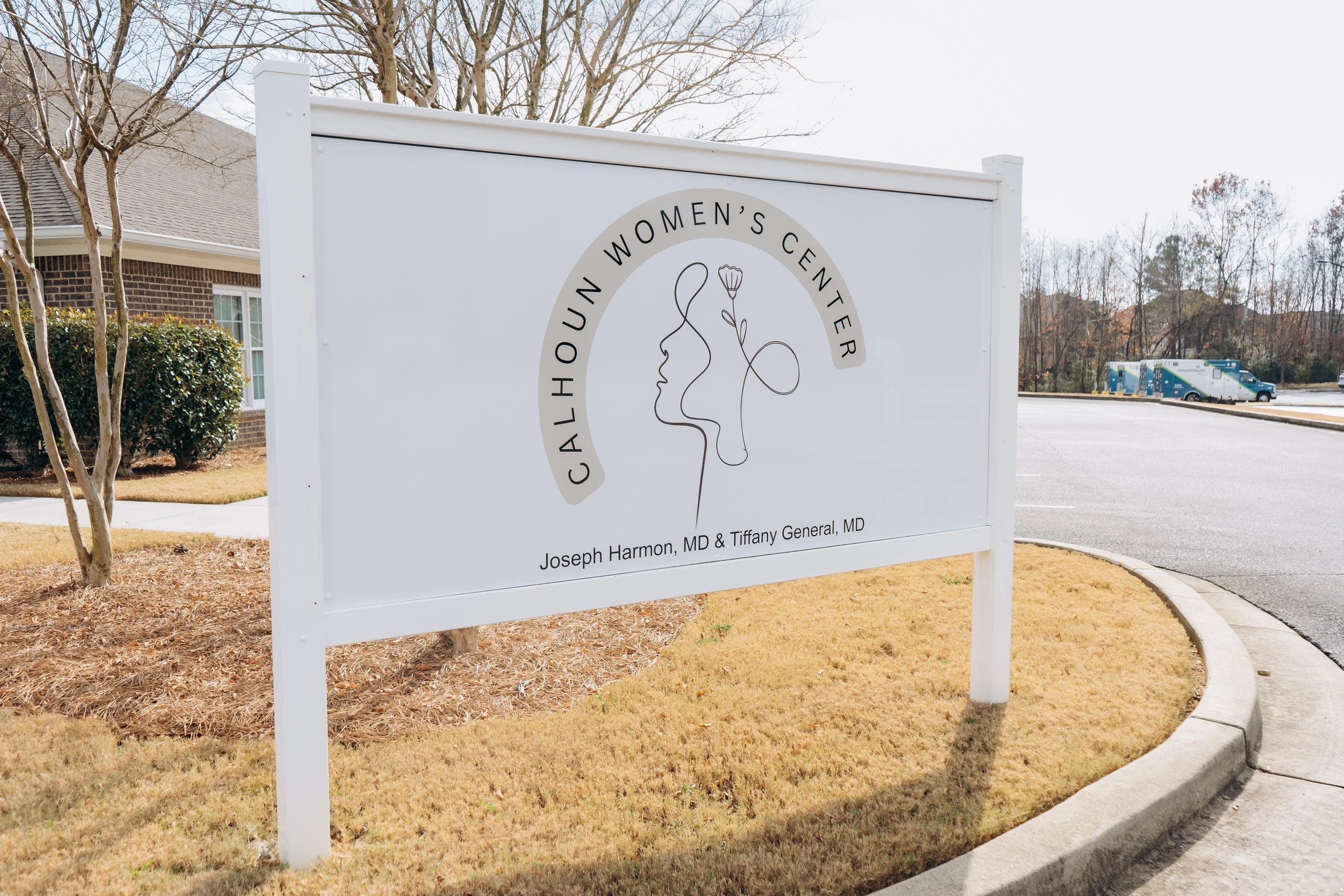Sign for Calhoun Women's Center with a line art of a woman and a flower, and text indicating it is run by Joseph Harmon, MD and Tiffany General, MD.