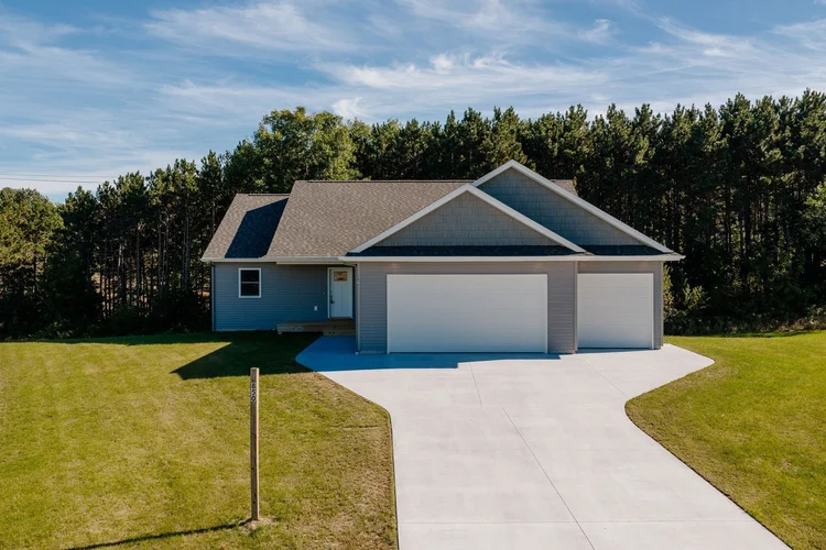 Front of home with concrete driveway and woods behind