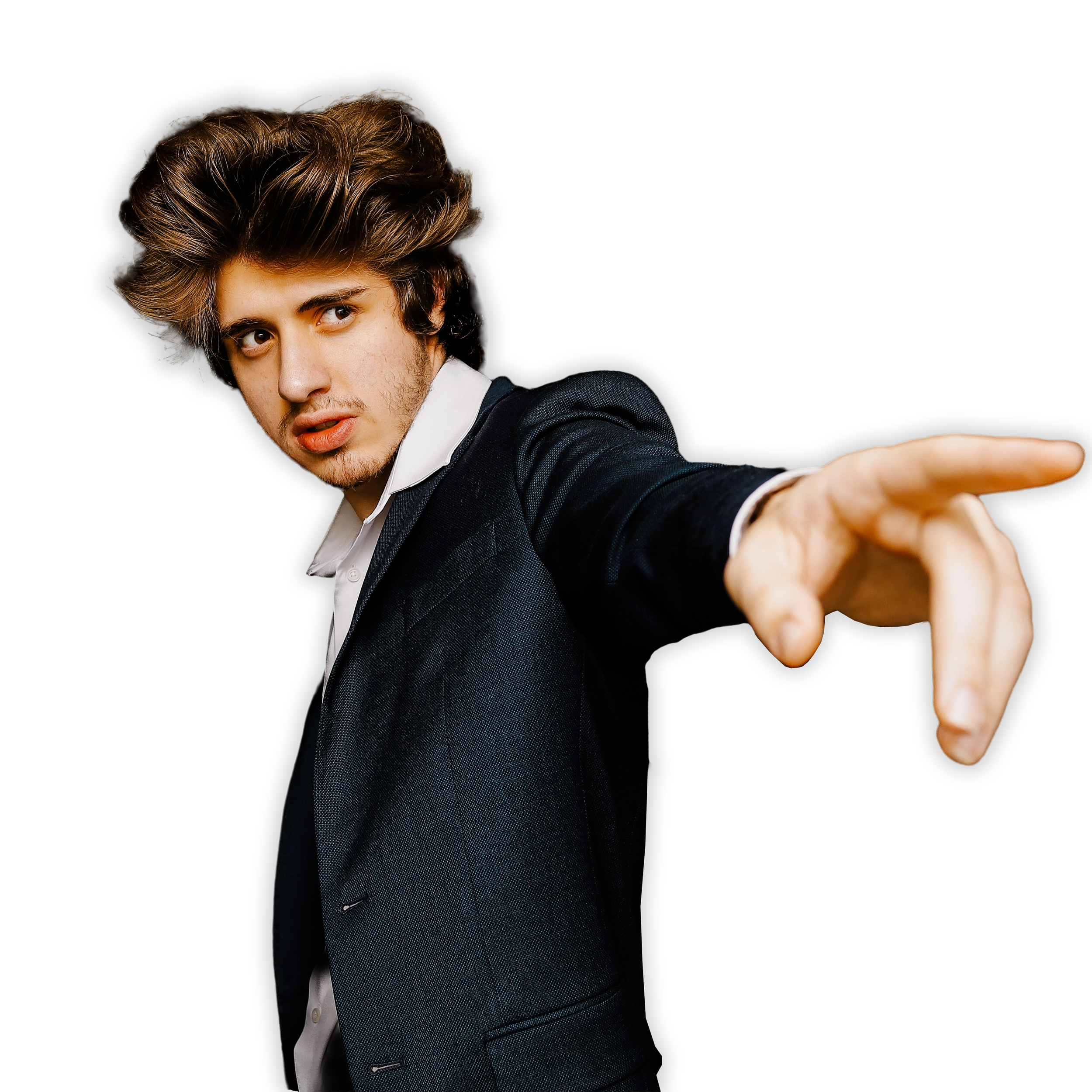 A young man with wavy brown hair and light skin dressed in a black suit and white shirt extending his arm forward against a black background.