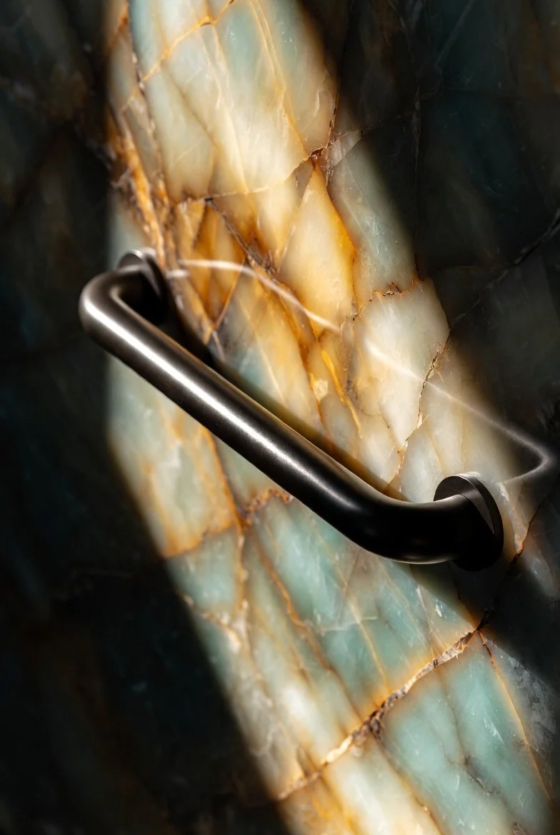 Close-up of a marble or onyx wall with a stainless steel handle or grab bar.