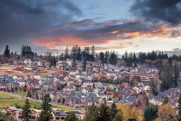 Suburban neighborhood with rows of houses, trees, and a colorful sunset sky with clouds. Happy Valley, OR.
