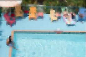 Personas descansando en sillas con paraguas en una piscina exterior