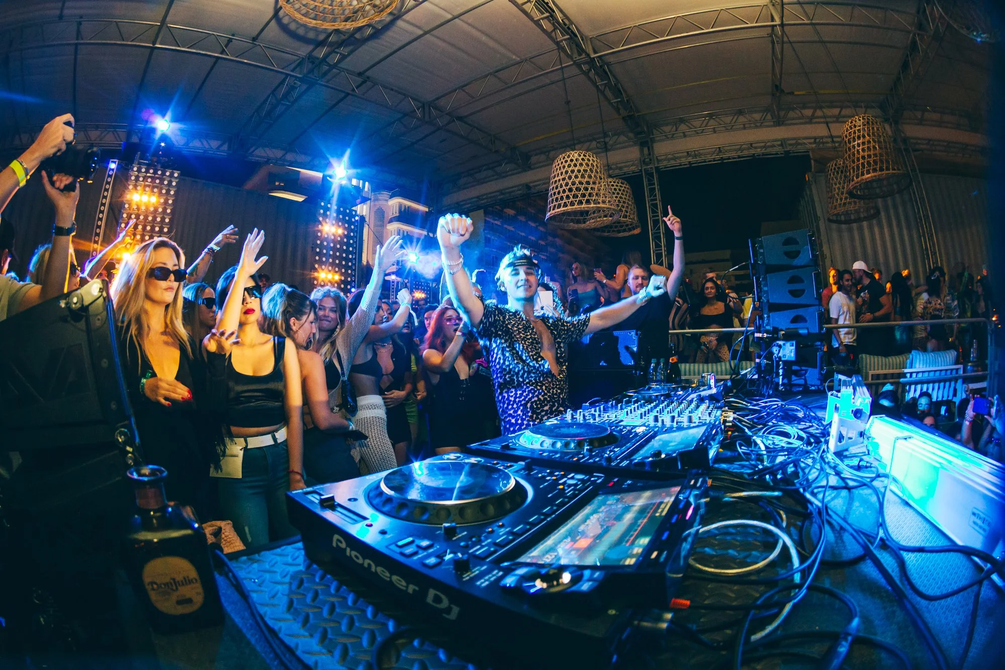 Una multitud de personas bailando y disfrutando en un evento en vivo, con DJ John Summit en el escenario y luces de colores en un espacio conocido como La Marketa.