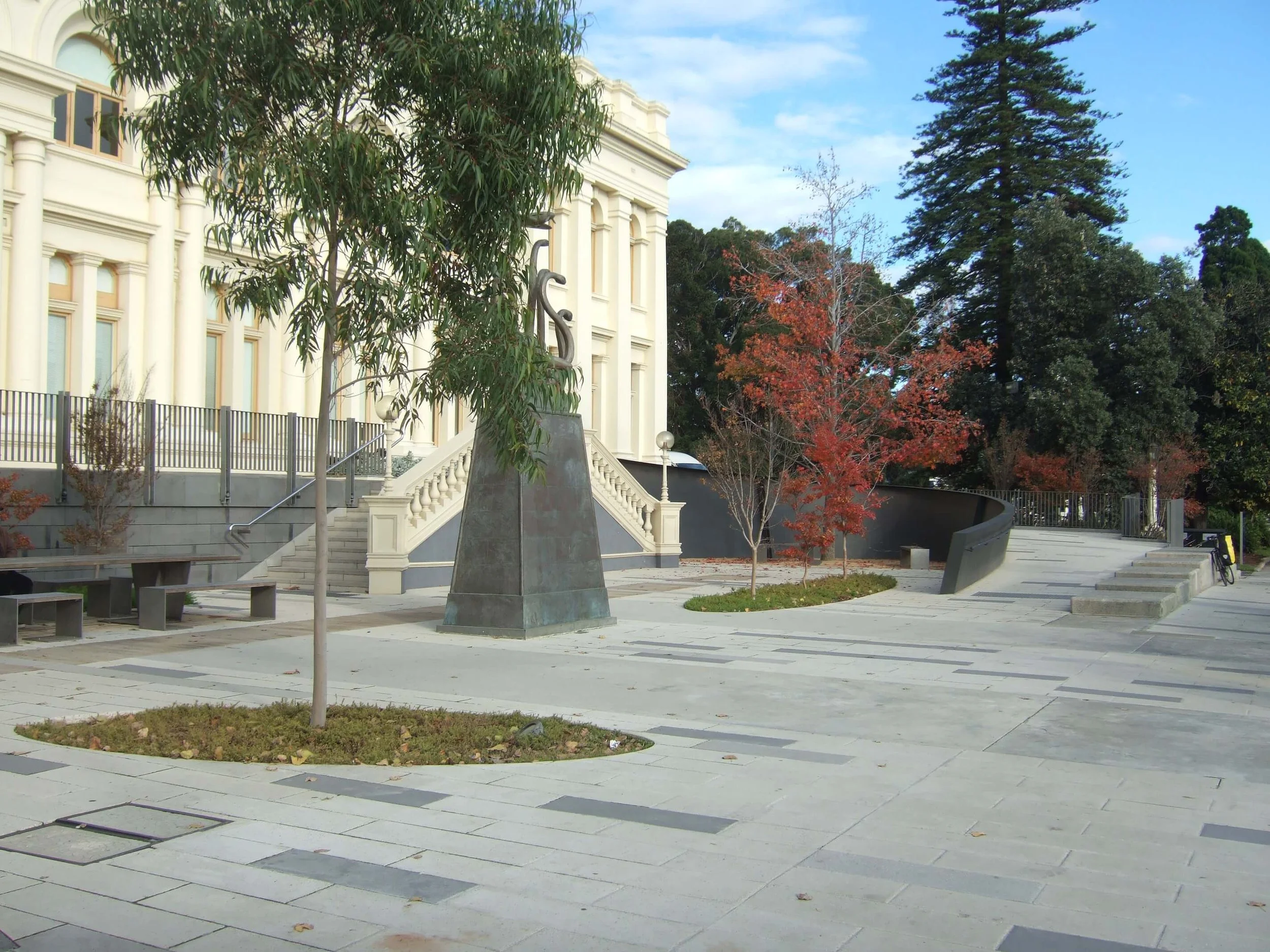Empty park with trees, a statue, stairs, and a historic building in the background on a clear day.