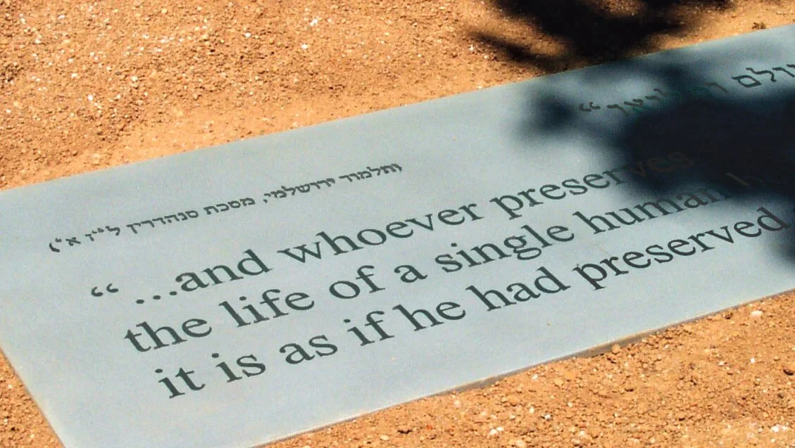 A plaque with an inscription resting on a gravel path and shadow partially covering it.
