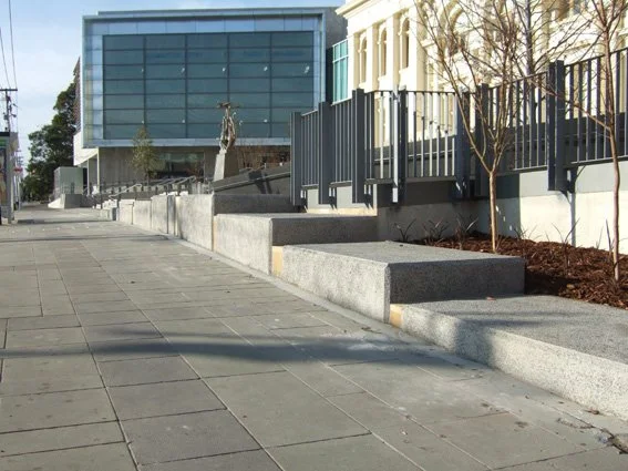 Empty sidewalk with concrete steps and a modern building with large glass windows in the background.