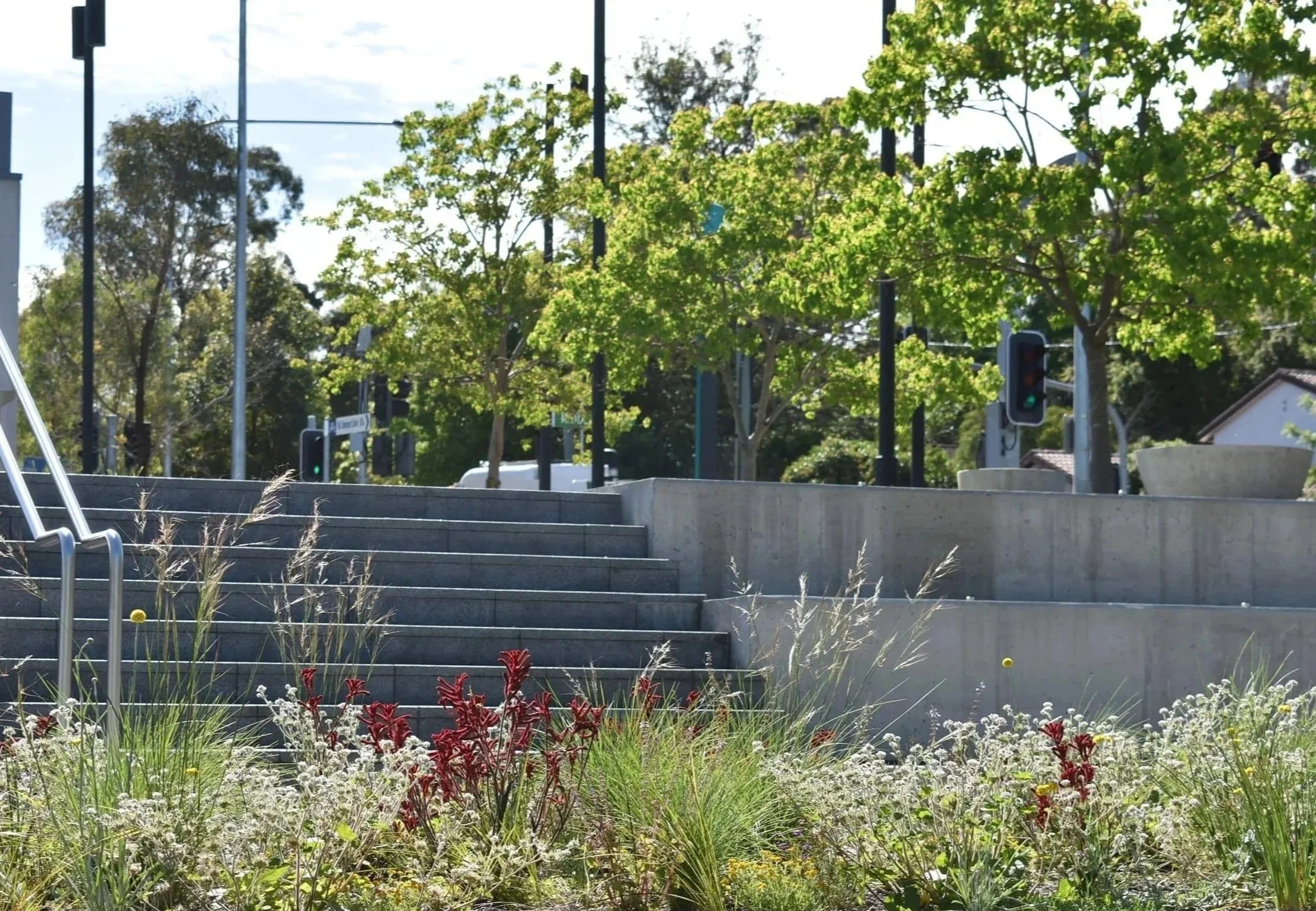 Concrete stairs and landing outdoors with greenery, trees, and traffic lights in the background.