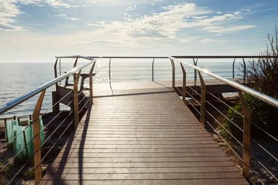 Wooden pier extending over water with railings, overlooking the ocean under a partly cloudy sky.