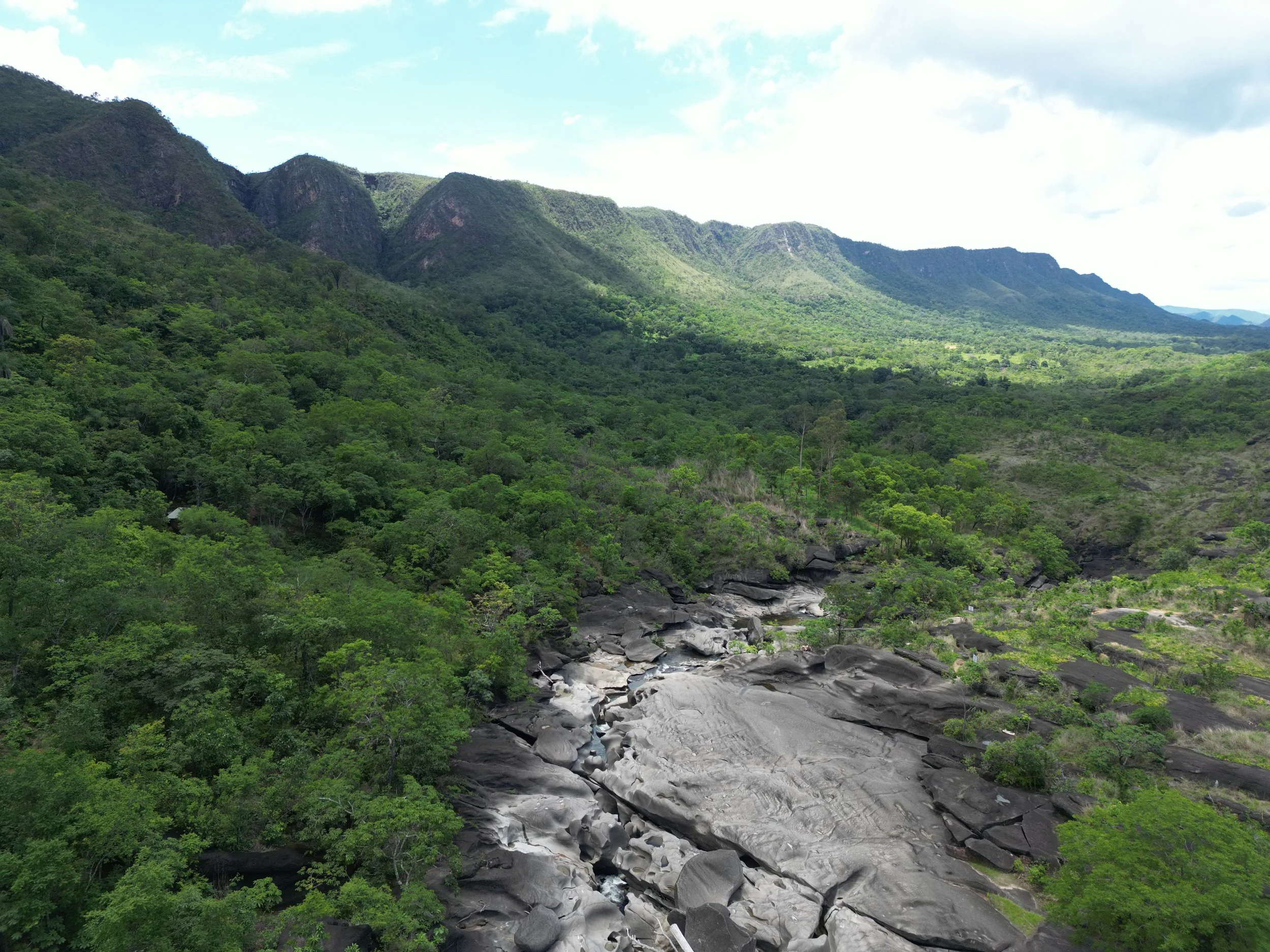 A lush green mountain landscape with a moonscape riverbed running through the forested area in Goias, Brazil.