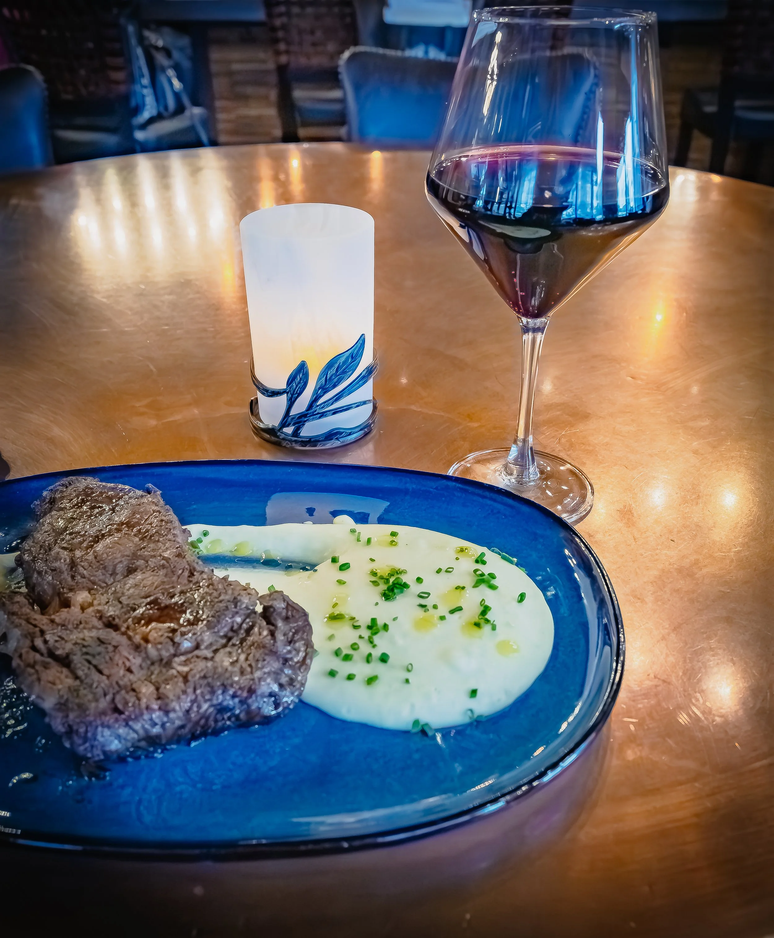 A plate of salad with mixed greens and fried eggplant slices, served with a glass of red wine, on a polished wooden table in a cozy restaurant setting.