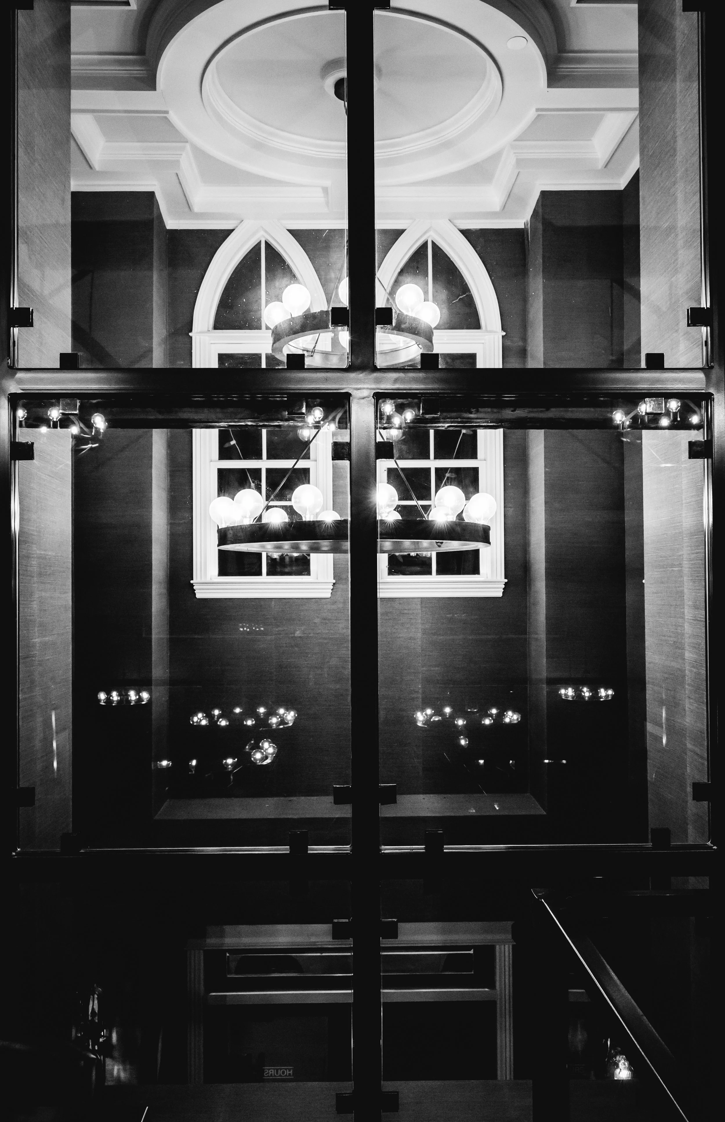 Black and white photo of a chandelier with round bulbs seen through a glass door.
