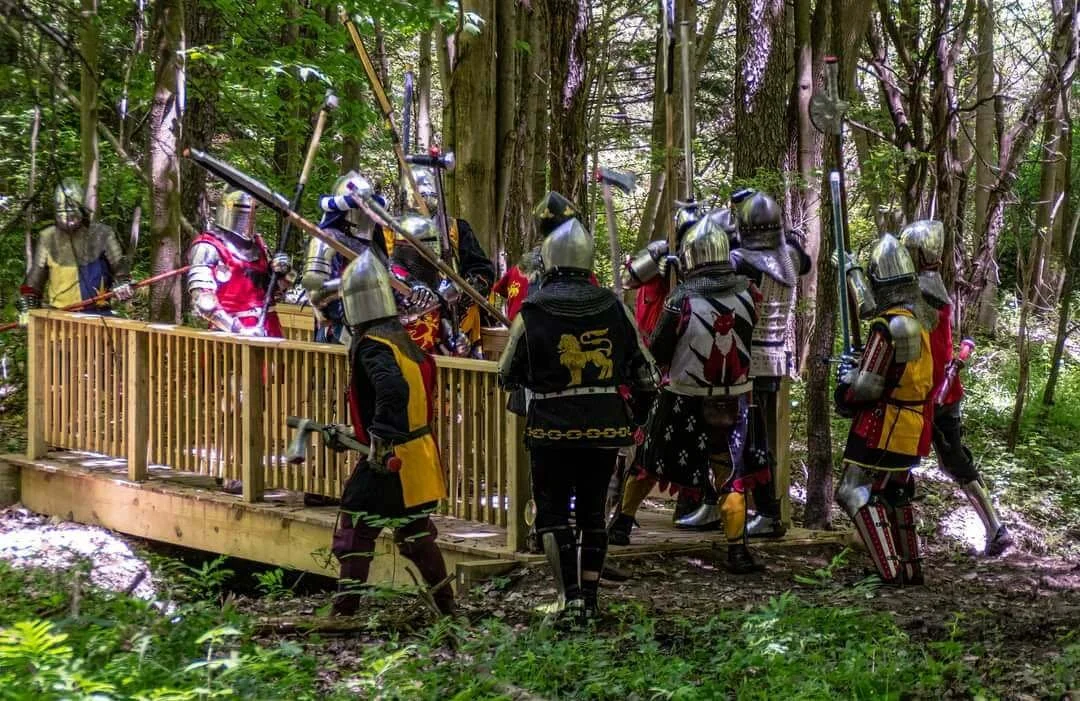 People dressed in medieval knight costumes with armor and helmets on a wooden platform in a forest.