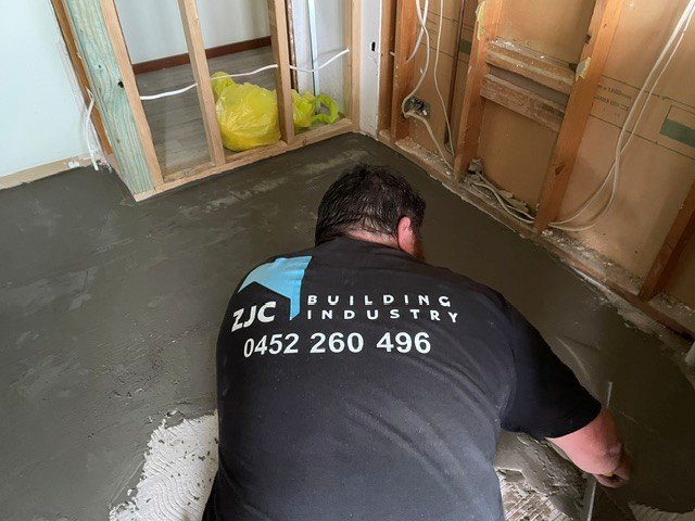 A person working on a concrete floor in a room under construction, with exposed wall studs and wiring.