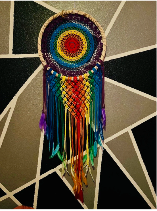 Colorful rainbow mandala dreamcatcher hanging on a wall with geometric black, white, and gray background.
