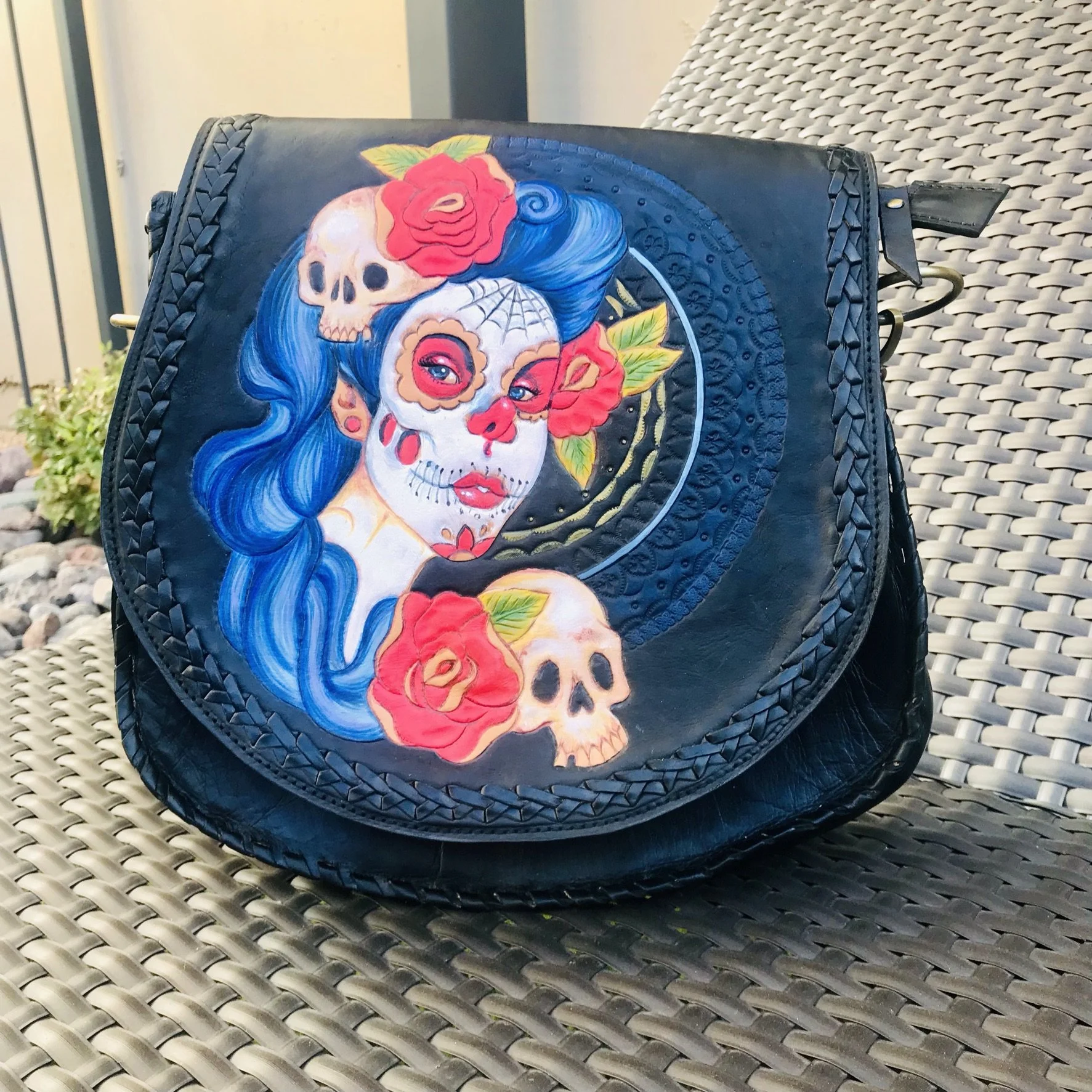 Black purse with colorful Day of the Dead style face painting of a woman with blue hair, surrounded by red roses and skulls.