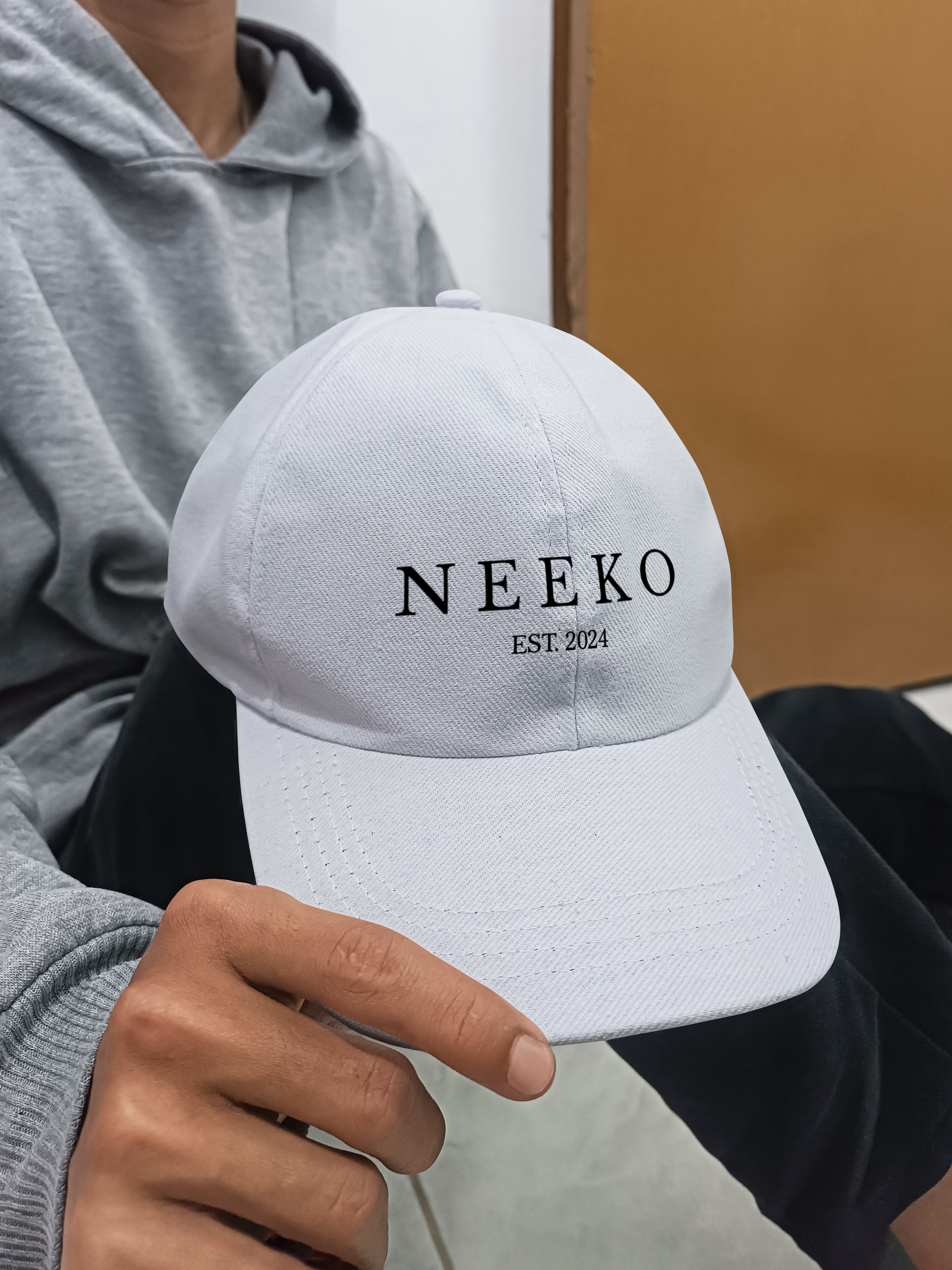 Person holding a white cap with the text "NEEKO EST. 2024" embroidered on the front.