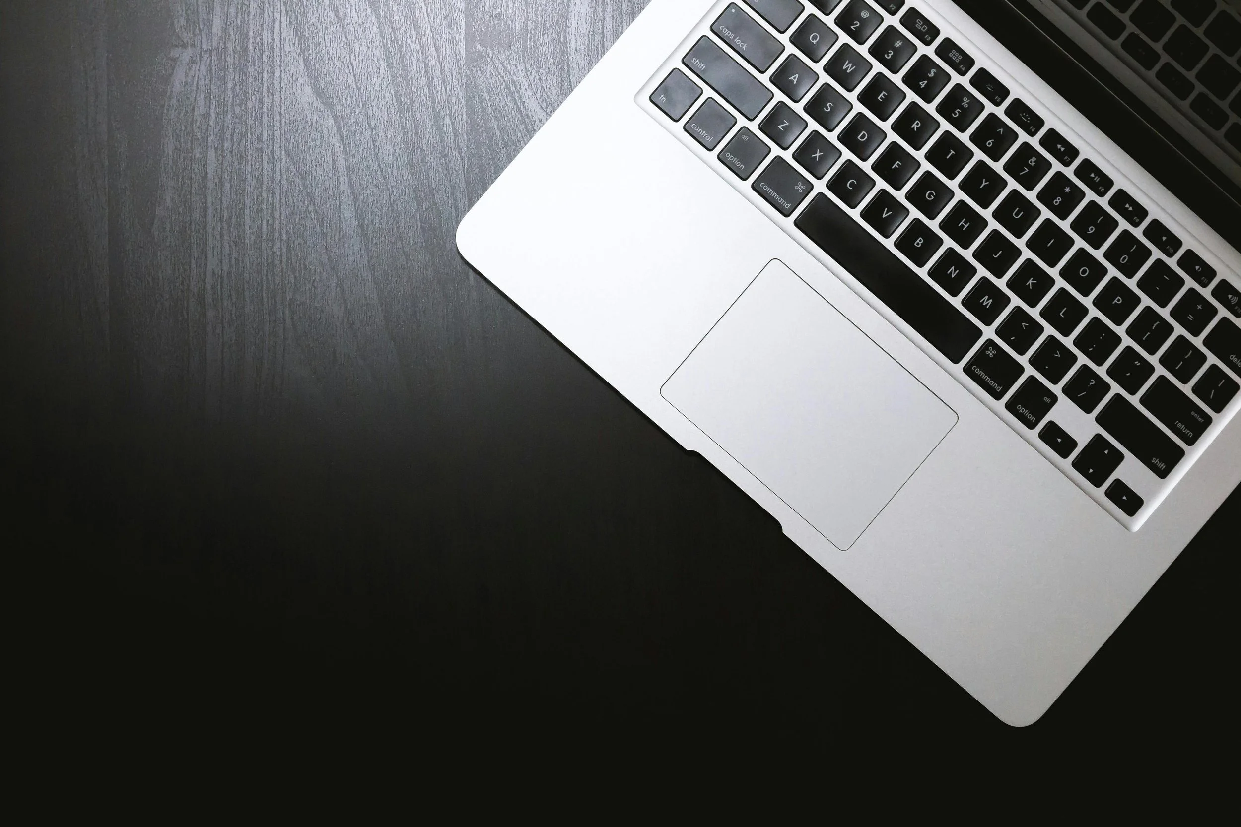 A silver laptop on a dark textured surface, with the keyboard and trackpad visible in the upper right corner.