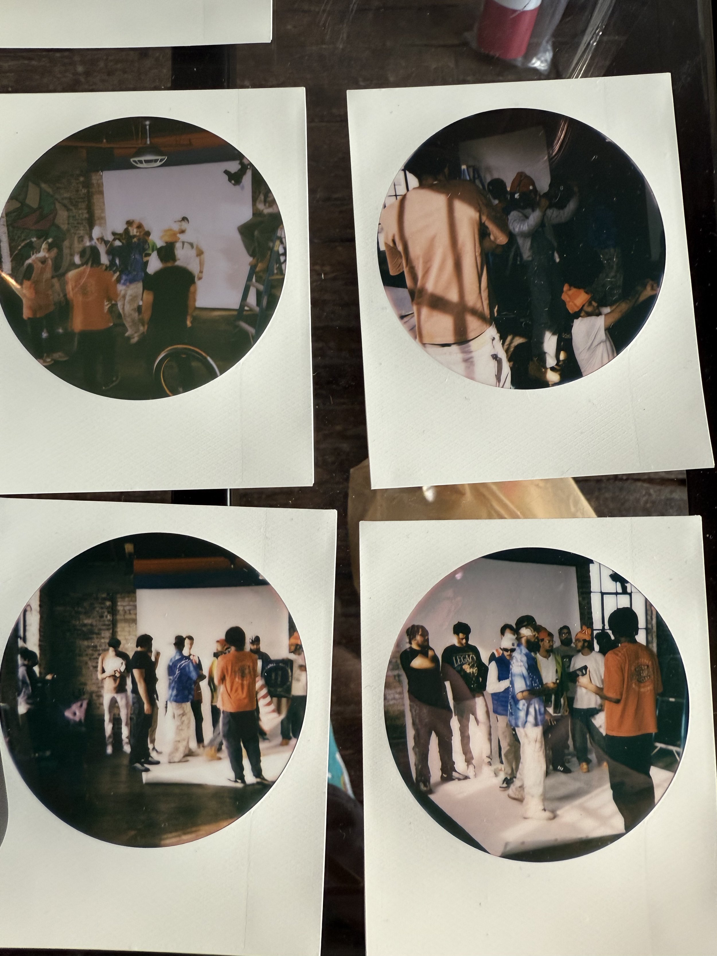 Four Polaroid photos showing a group of people in a studio with a white backdrop, engaging in various activities like taking photos and rehearsing.