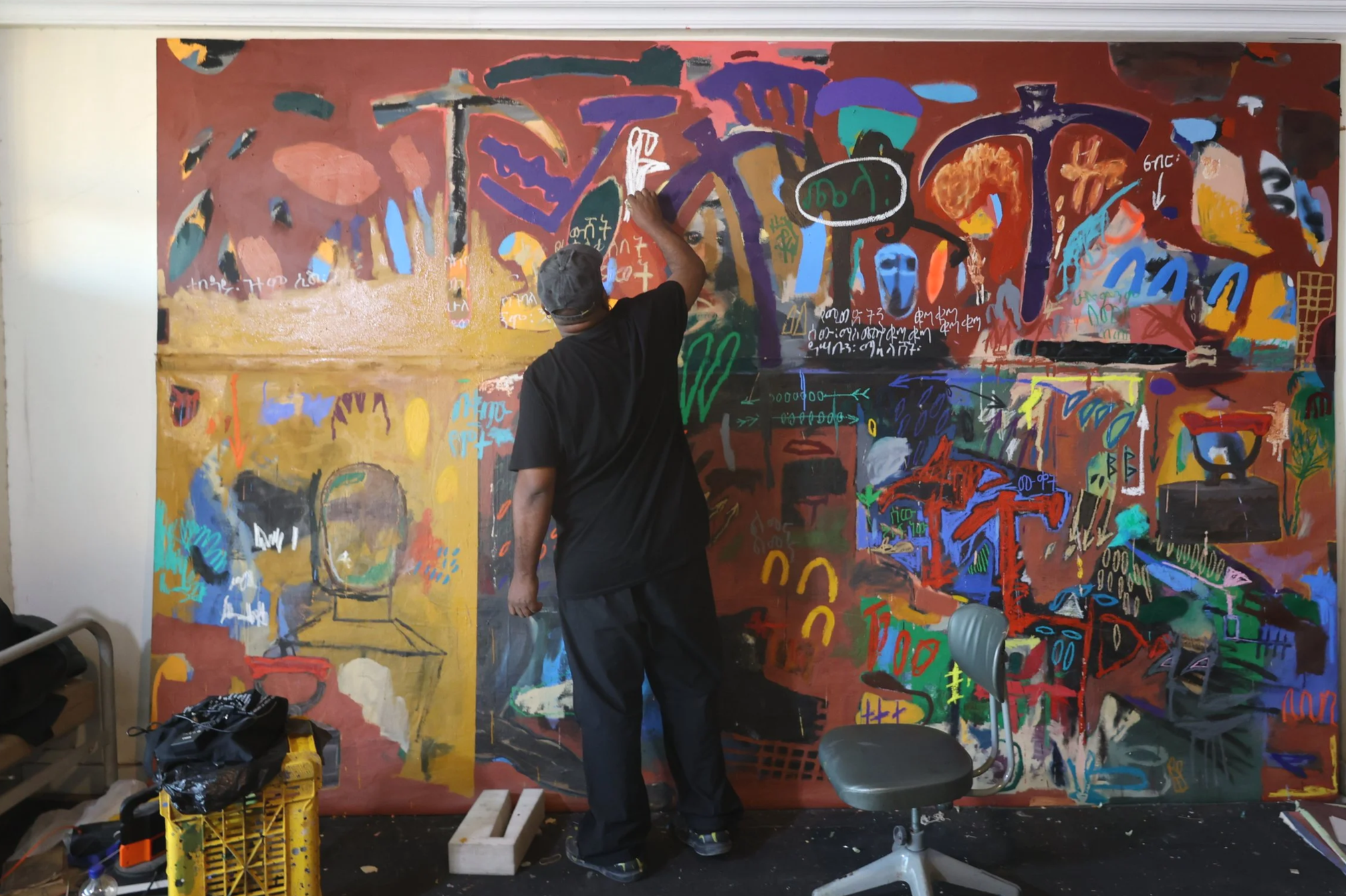 An artist creates abstract graffiti art on a large wall with a variety of colors and shapes.