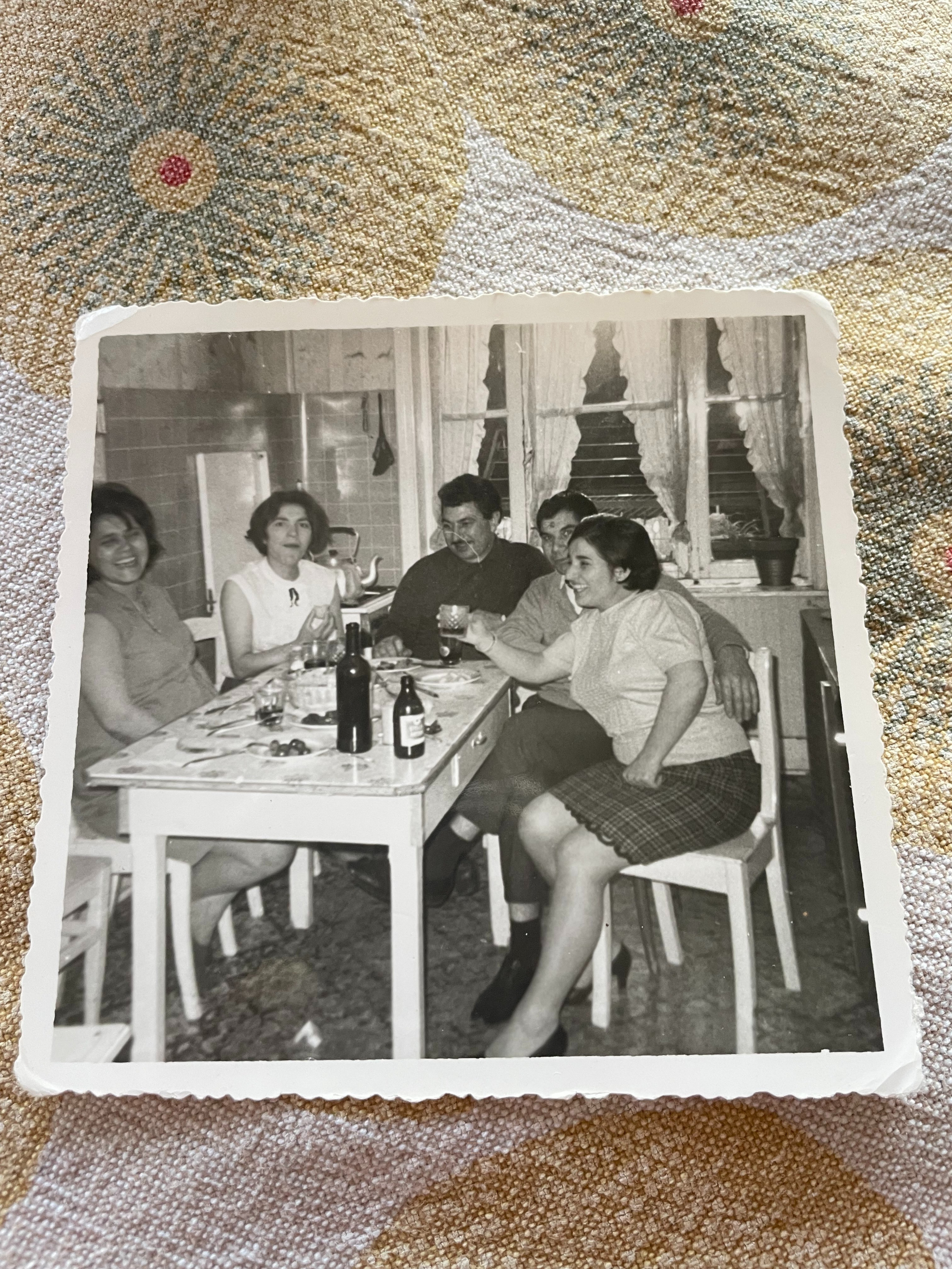 A B&W photo of my yiayia sitting around a dining table with family members, in the family home kitchen at Rue Vandeweyer 78 in Schaarbeek, ca. 1973.