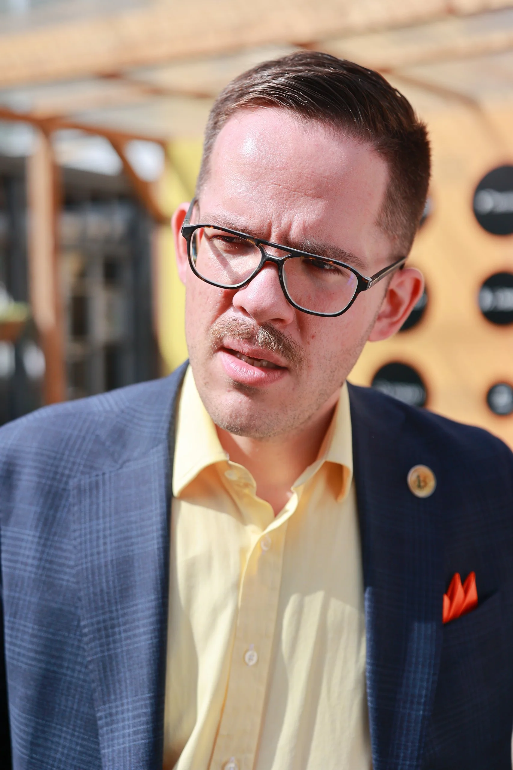 A man with glasses, a yellow shirt, and a blue blazer making a confused or disgusted facial expression.