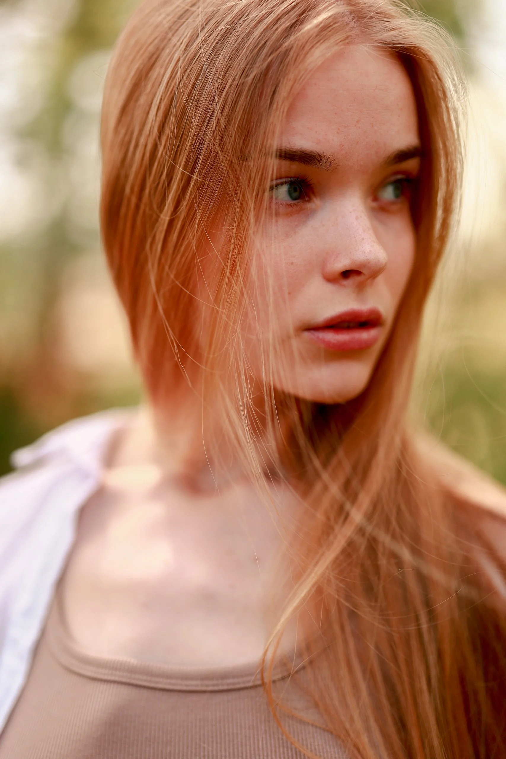 Close-up of a young woman with long red hair and freckles looking to the side outdoors.